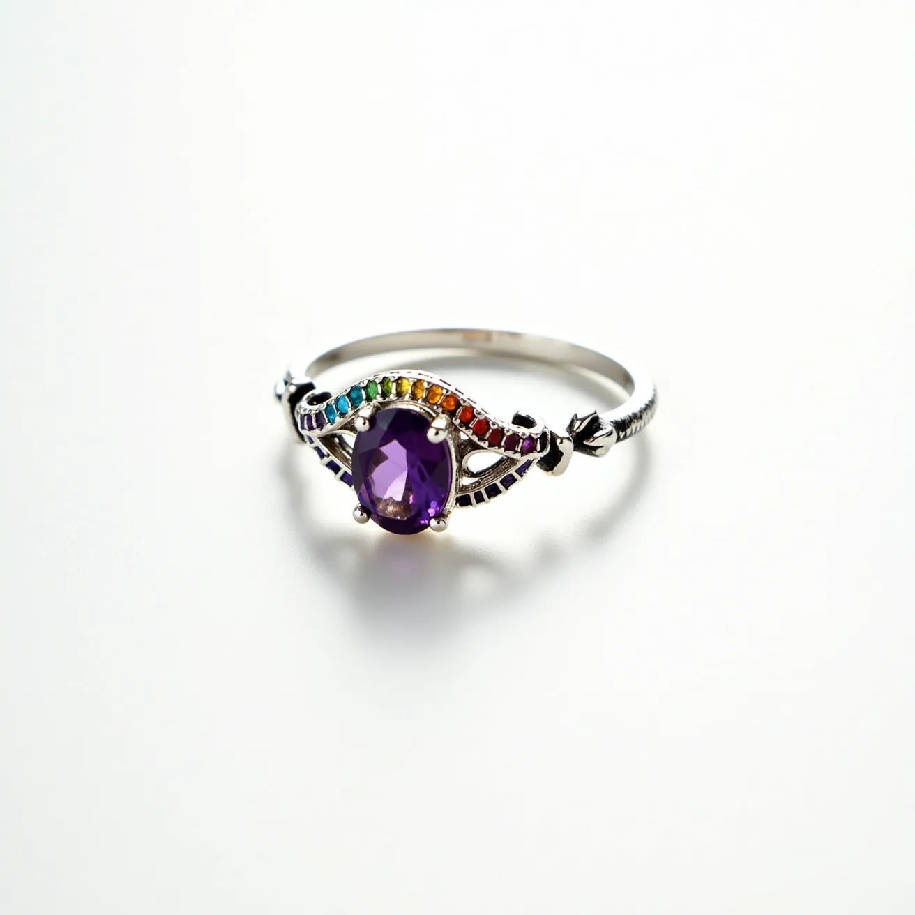 This rainbow ring features a prominent oval-cut purple gemstone, set in a four-prong setting at its center. The band appears to be made of a silvery metal, possibly sterling silver or white gold, and is adorned with a series of small, multicolored gemstones arranged in a rainbow pattern along the top side, enhancing the vibrant appearance. The colorful stones are likely a mix of sapphires or other vibrant gems, each set in a channel setting that complements the main gem's brilliance. The ring's design is both elegant and playful, making it a striking piece of jewelry.