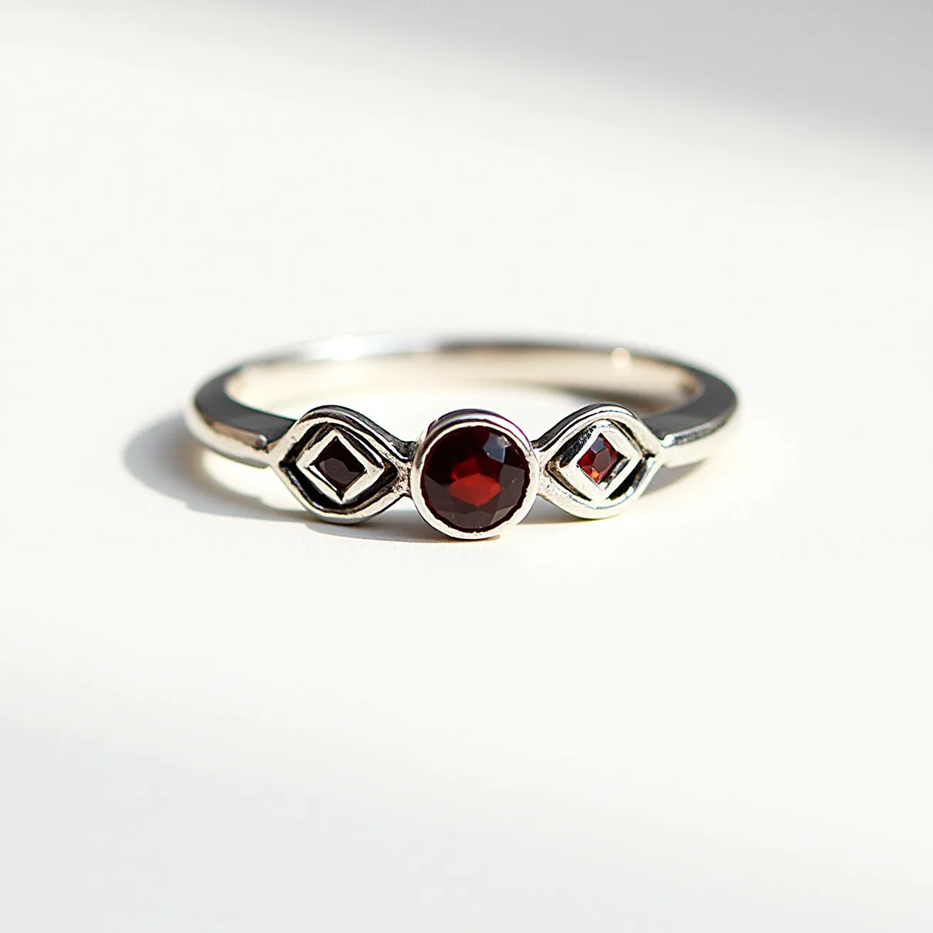 This rainbow ring features a sleek metal band, likely made of silver or white gold, with a central round-cut red gemstone securely set in a bezel setting. Flanking the main stone are two smaller diamond-shaped red stones set within stylized geometric frames, possibly reflecting a modern design. The arrangement highlights a balance of symmetry and elegance, making it a versatile piece for various occasions. The absence of a clasp indicates it is a slip-on style, typical for rings.