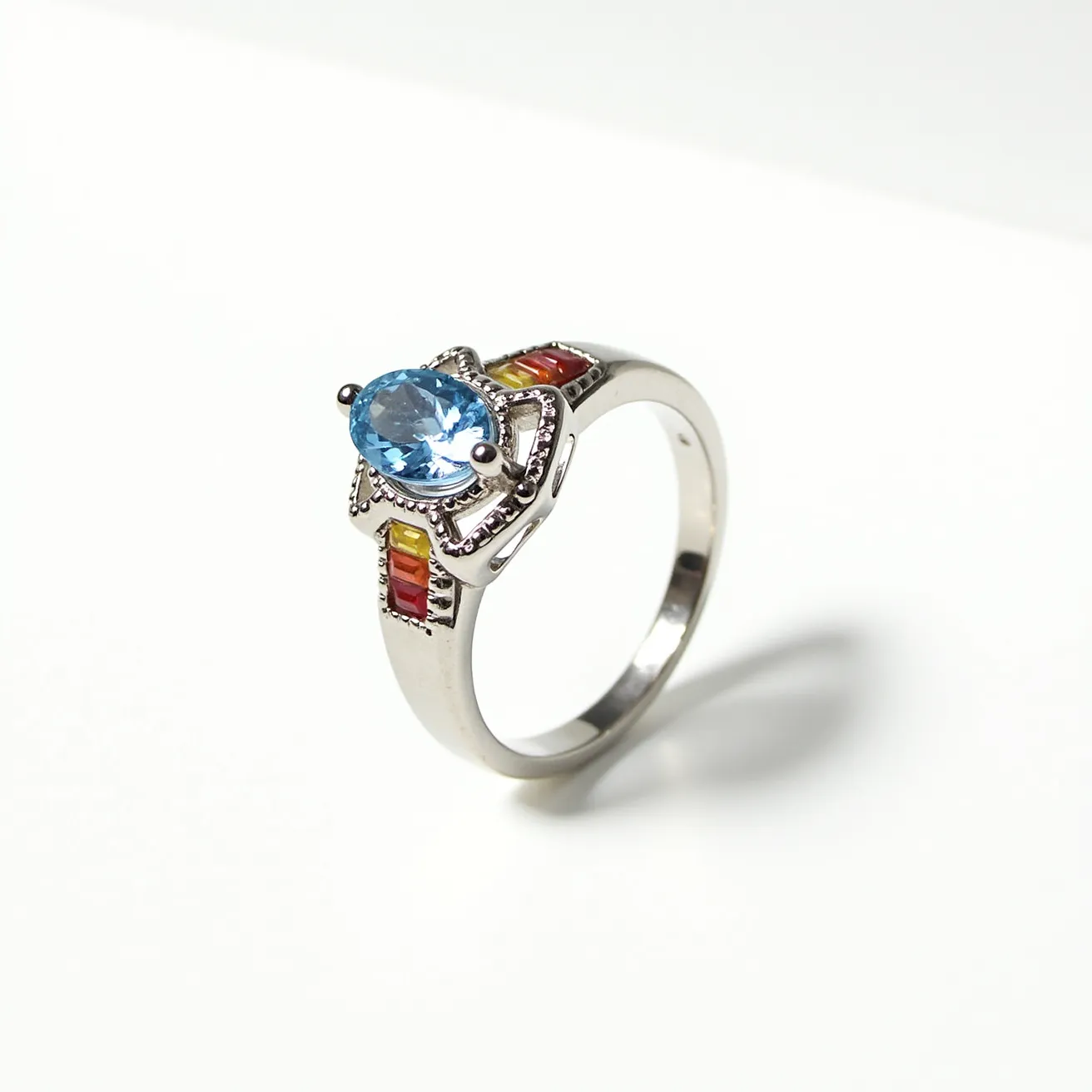 This rainbow ring features a silver band with a prominent oval-cut blue gemstone, likely topaz, securely held in place by a prong setting. The band is adorned with small rectangular gemstones in shades of red, yellow, and orange, channel-set along the sides, adding a vibrant spectrum of color. The intricate details surrounding the central stone enhance its elegance, while the smooth finish of the silver complements the overall design. The combination of carefully selected gemstones arranged in a rainbow pattern alongside the larger central stone creates a striking and harmonious aesthetic.