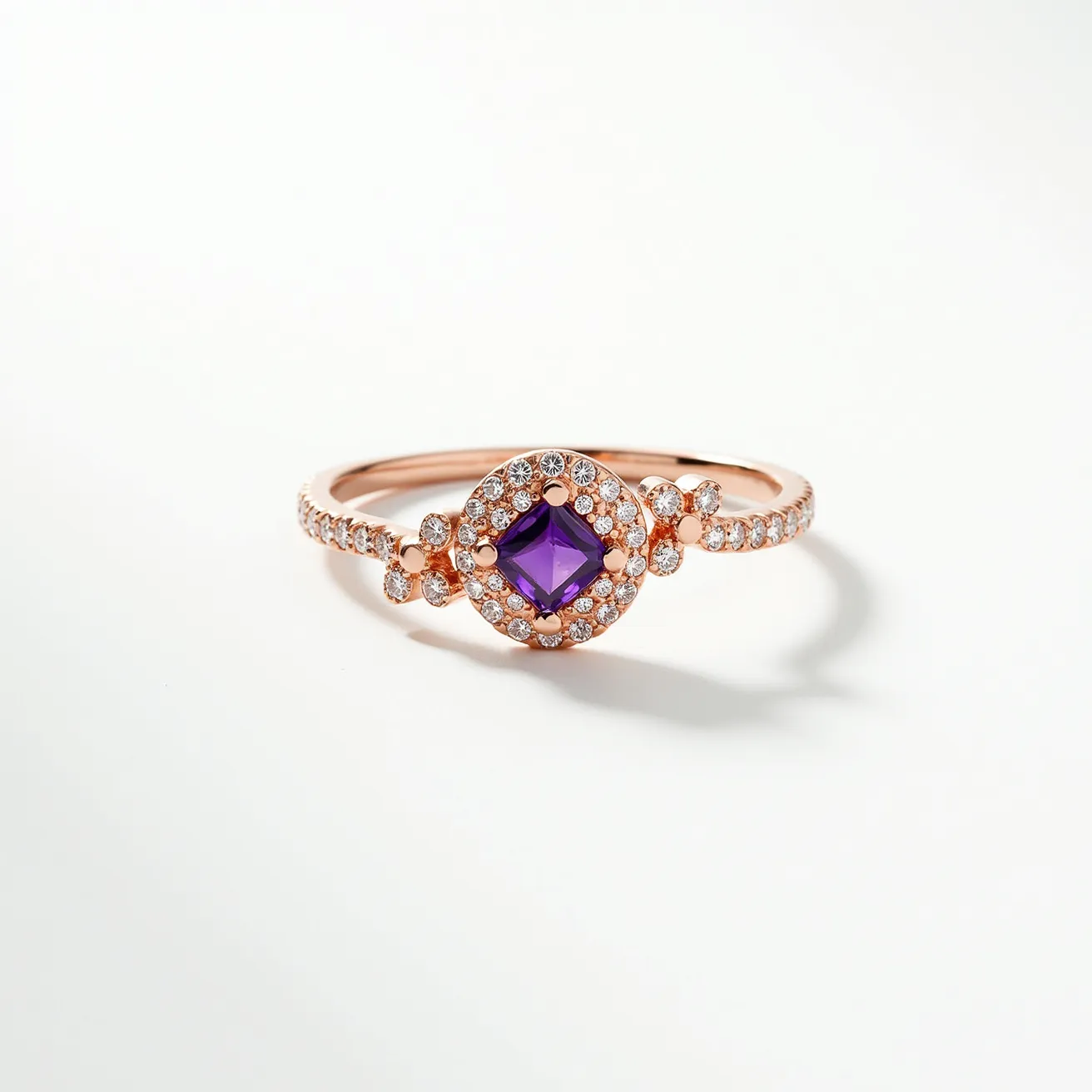 This Rapunzel ring is crafted from rose gold, creating a warm and rich backdrop for the centerpiece. At the heart of the ring lies a square-cut purple gemstone, likely an amethyst, which adds a regal touch. The central stone is surrounded by a halo of small, sparkling clear stones, possibly diamonds or cubic zirconia, set in a pavé style. These stones extend halfway down the band on either side, enhancing the overall brilliance and elegance of the piece. The ring does not feature any clasps, as it is designed to be a fixed band for easy wear.