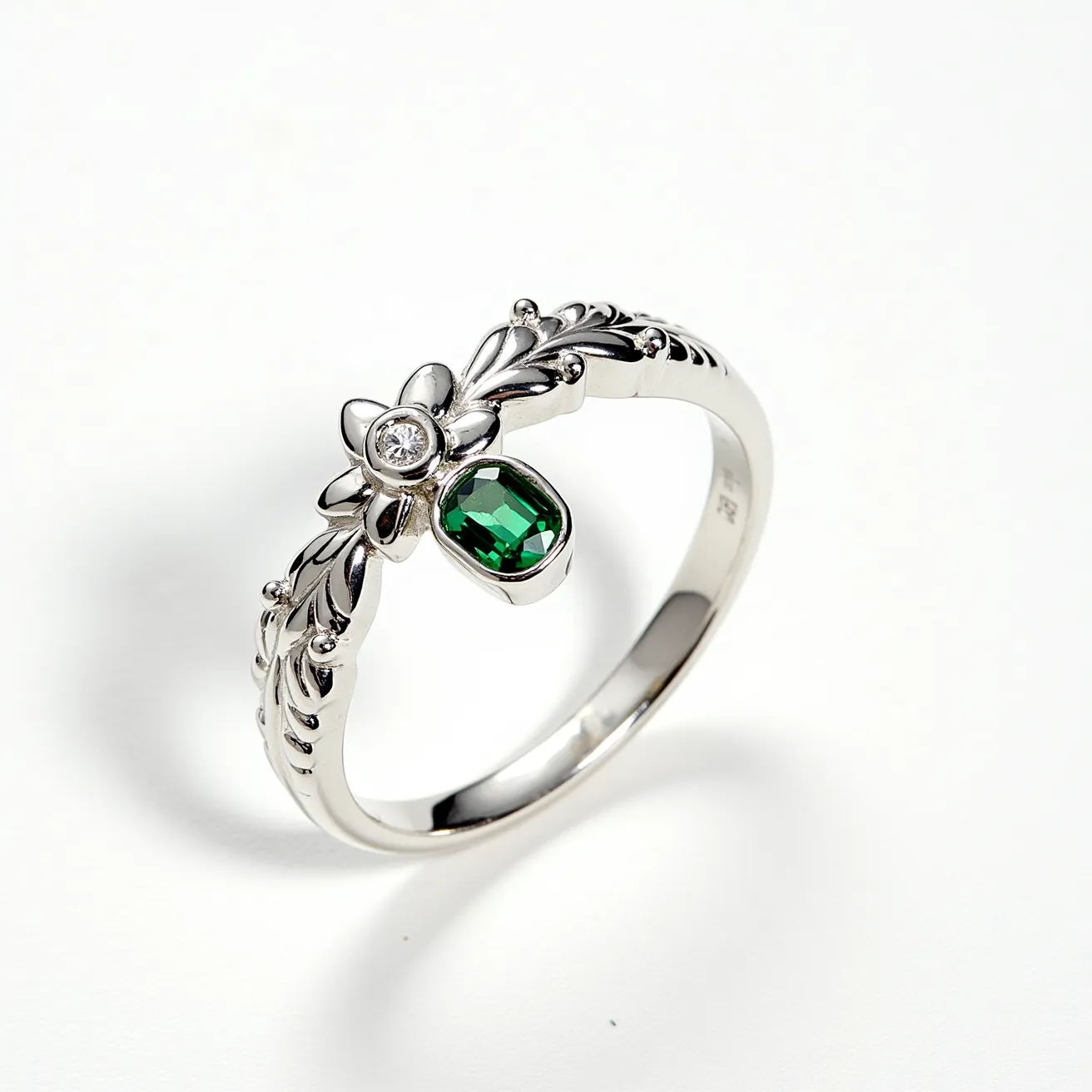 This Rapunzel ring features an intricately designed white metal band, likely made of silver or white gold, with a leaf motif along its circumference. It showcases a brilliant round-cut white gemstone, possibly a diamond or cubic zirconia, set in a prong setting atop a flower design. Adjacent to this is a dangling oval green gemstone with a faceted cut, secured in a bezel setting, adding a touch of whimsy to the piece. The ring captures a sense of enchantment reminiscent of the Rapunzel story, combining natural elements with elegant craftsmanship.