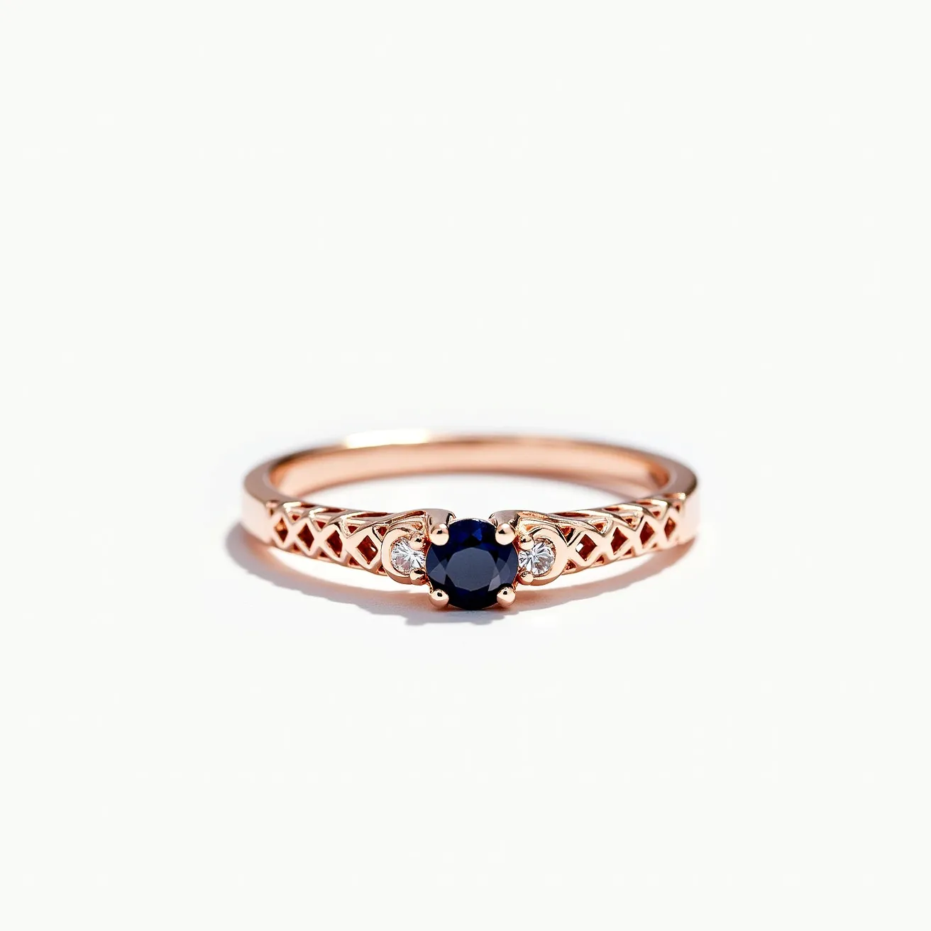 This ring band features a delicate, lattice-patterned design crafted from rose gold. At its center is a round-cut blue sapphire, held securely by four prongs, showcasing its deep, rich hue. On either side of the sapphire, small round-cut diamonds are set, enhancing the dazzle of the central stone and adding an elegant contrast. The combination of the intricate band and the vivid sapphire with sparkling diamonds gives the ring a sophisticated and timeless appeal.