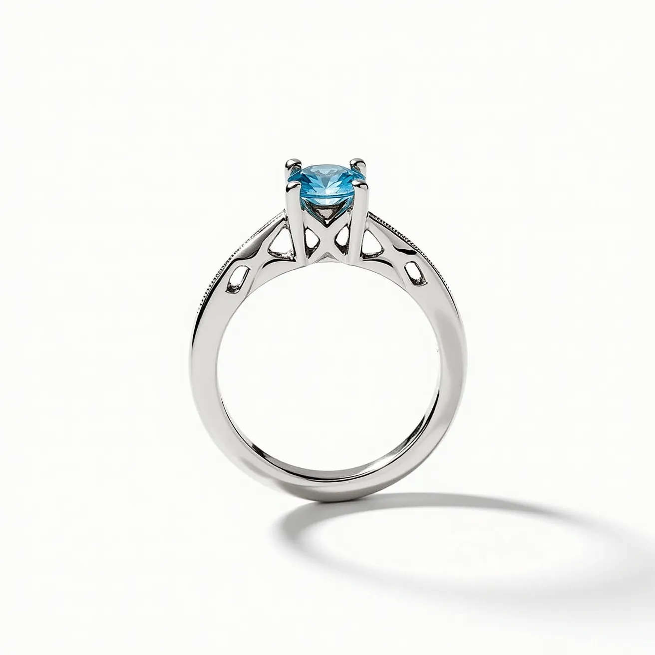 This ring band is elegantly crafted, featuring a sleek and polished metal setting that appears to be made of a white metal, likely white gold or platinum. It is adorned with a striking blue gemstone cut in a round shape, securely held in place by a four-prong setting. The prong setting elevates the gemstone, allowing light to enhance its brilliance. The band itself is embellished with intricate filigree work, adding a touch of sophistication and artistry to the overall design.