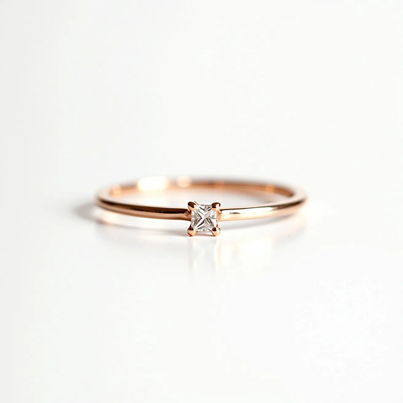 This ring band features a delicate and minimalist design crafted from a warm-toned metal, likely rose gold. It showcases a central gem, specifically a small, square-cut diamond or similar stone, set in a prong setting that securely holds the gemstone. The choice of a square cut adds a modern touch to the classic elegance of the ring. The band is slender and unembellished, drawing focus to the brilliance of the gemstone itself. This simplistic design highlights both the material of the band and the sparkle of the gem harmoniously.