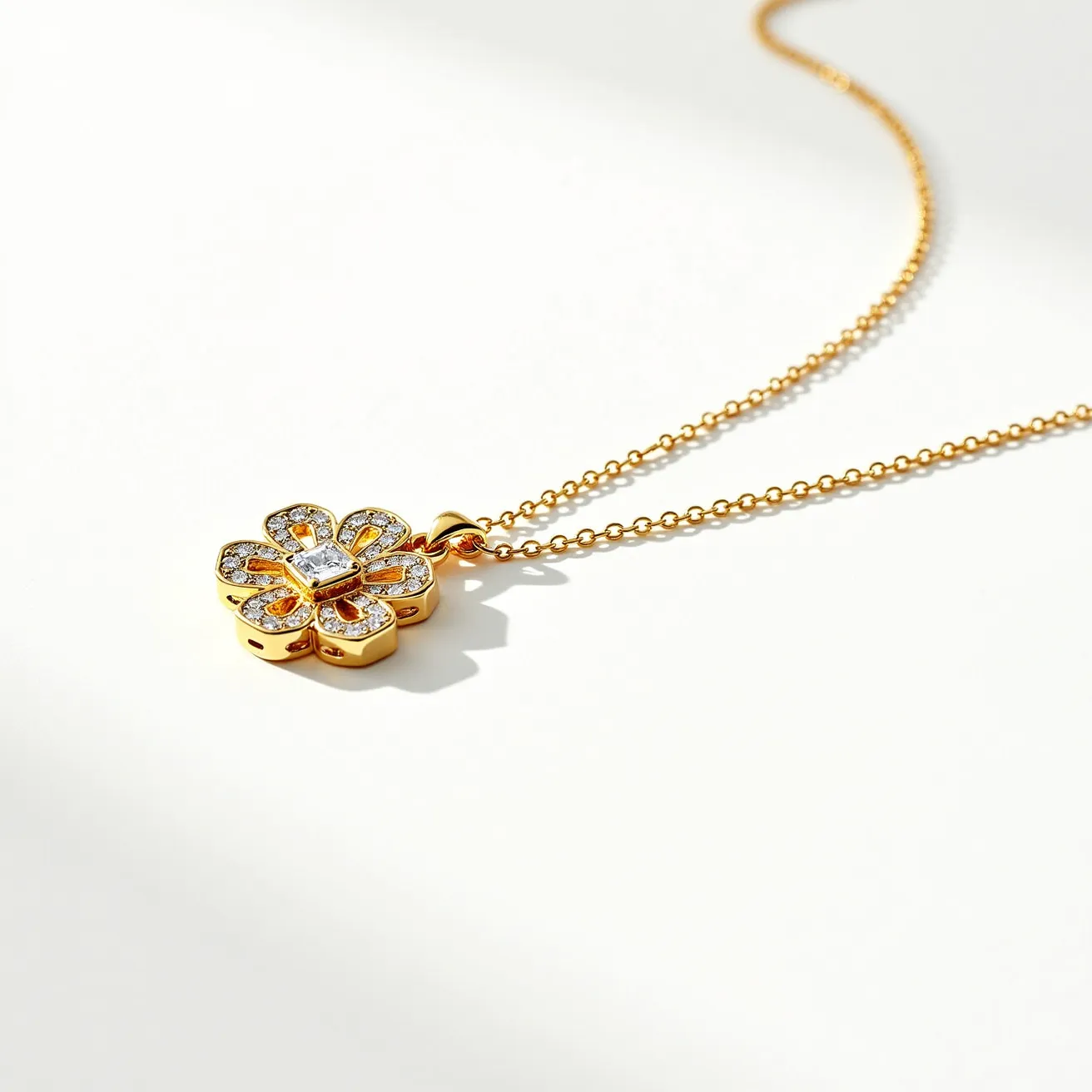 This ring necklace features a delicate pendant designed in the shape of a flower, crafted from a gold-toned metal that complements the overall elegance of the piece. The petals are adorned with small, round-cut, clear stones that appear to be diamonds, set in a pave style that maximizes their sparkle. At the center of the flower, there is a larger, square-cut stone, which adds a focal point to the design. The pendant hangs from a fine, gold-toned chain with a simple yet secure loop clasp that ensures the necklace stays comfortably in place when worn.