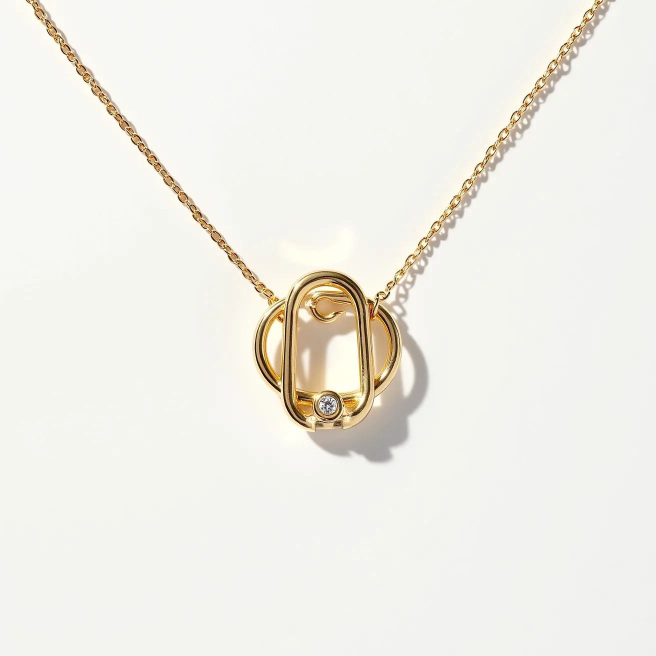 This ring necklace features a series of interconnected gold-toned rings, one of which includes a small, round-cut gemstone set into its surface, adding a touch of elegance and sparkle. The setting of the stone appears flush with the metal, securely held in place. The necklace chain exhibits a fine, delicate design that complements the pendant's sleek appearance. The clasp or attachment mechanism is a simple hook, seamlessly integrated to maintain the minimalist aesthetic of the piece.