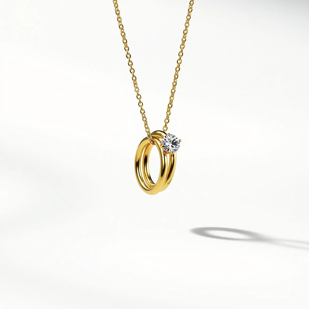 This ring necklace features a delicate gold chain suspending two interlocked gold rings. Attached to one of the rings is a sparkling, round-cut gemstone, likely a diamond, which is set in a classic prong setting that enhances its brilliance. The simplicity of the gold rings contrasts elegantly with the dazzling stone, creating a timeless and sophisticated accessory. The chain appears to have a standard clasp for secure attachment, complementing the overall design with its understated elegance.