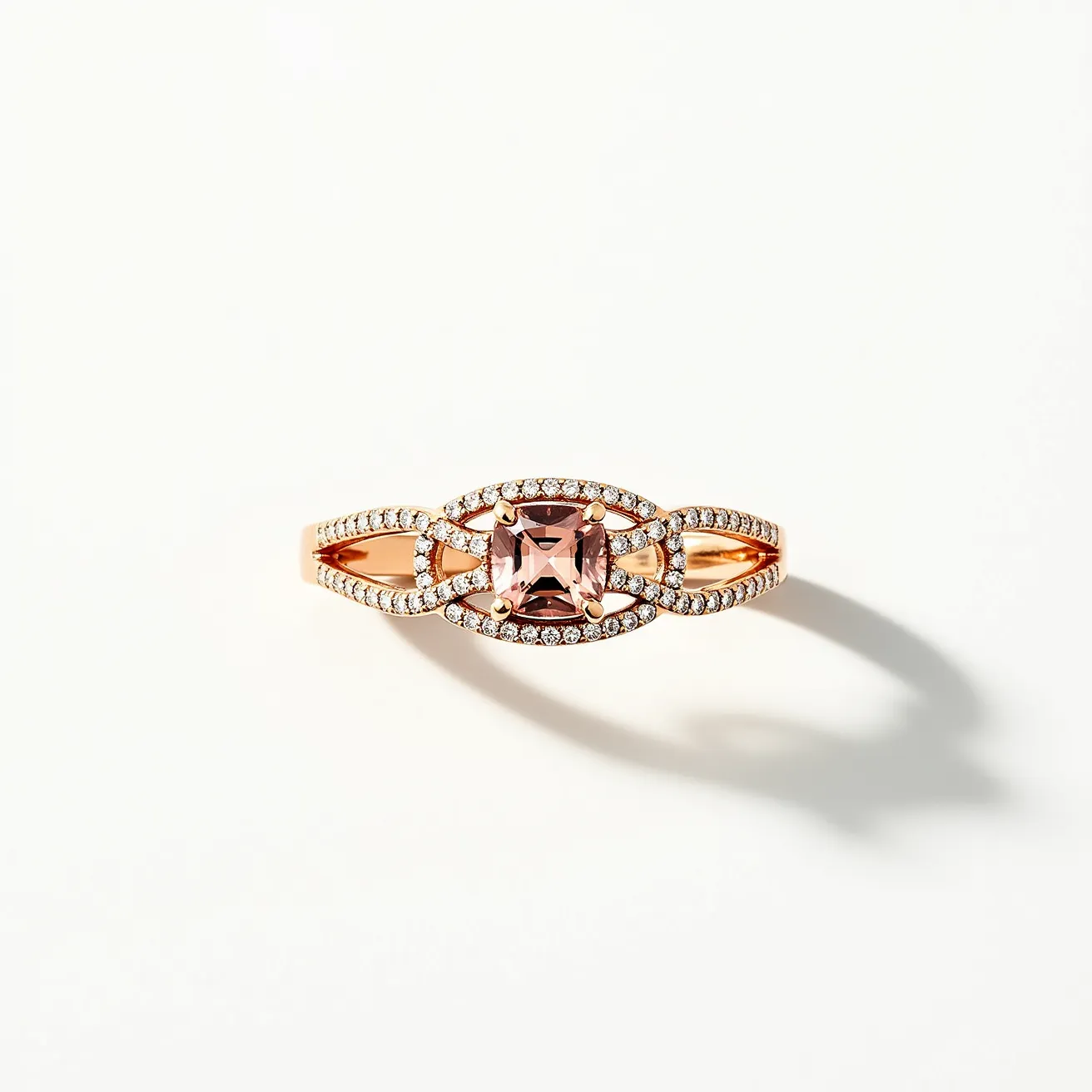 This rose gold ring features an intricate design centered around a cushion-cut gemstone, likely a pink morganite, held in place by four prongs. Surrounding the central gem is a delicate arrangement of small, sparkling diamonds set in a halo and extending along the band, lending the ring an elegant and timeless appeal. The band itself is crafted from rose gold, adding warmth and sophistication to the overall look. The intricate detailing of the band further enhances its beauty, creating a striking balance between the central gem and the surrounding accents.