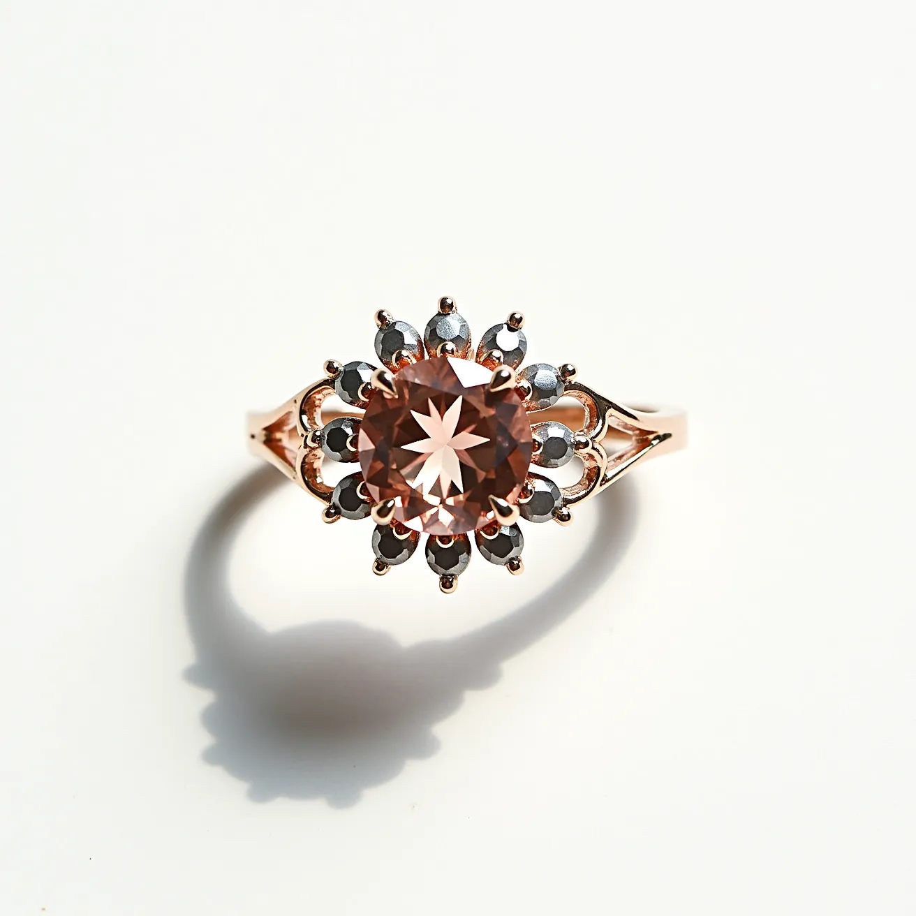 This rose gold ring features a striking central gemstone, cut in a round brilliant style, showcasing a warm, pinkish hue characteristic of morganite. The central stone is surrounded by a halo of smaller round dark stones, possibly black diamonds or sapphires, set in an intricate floral design. The ring band, crafted from rose gold, elegantly splits near the setting, adding a delicate architectural element that enhances the overall aesthetic. The stones are securely held in place with sturdy prongs, ensuring both durability and style.