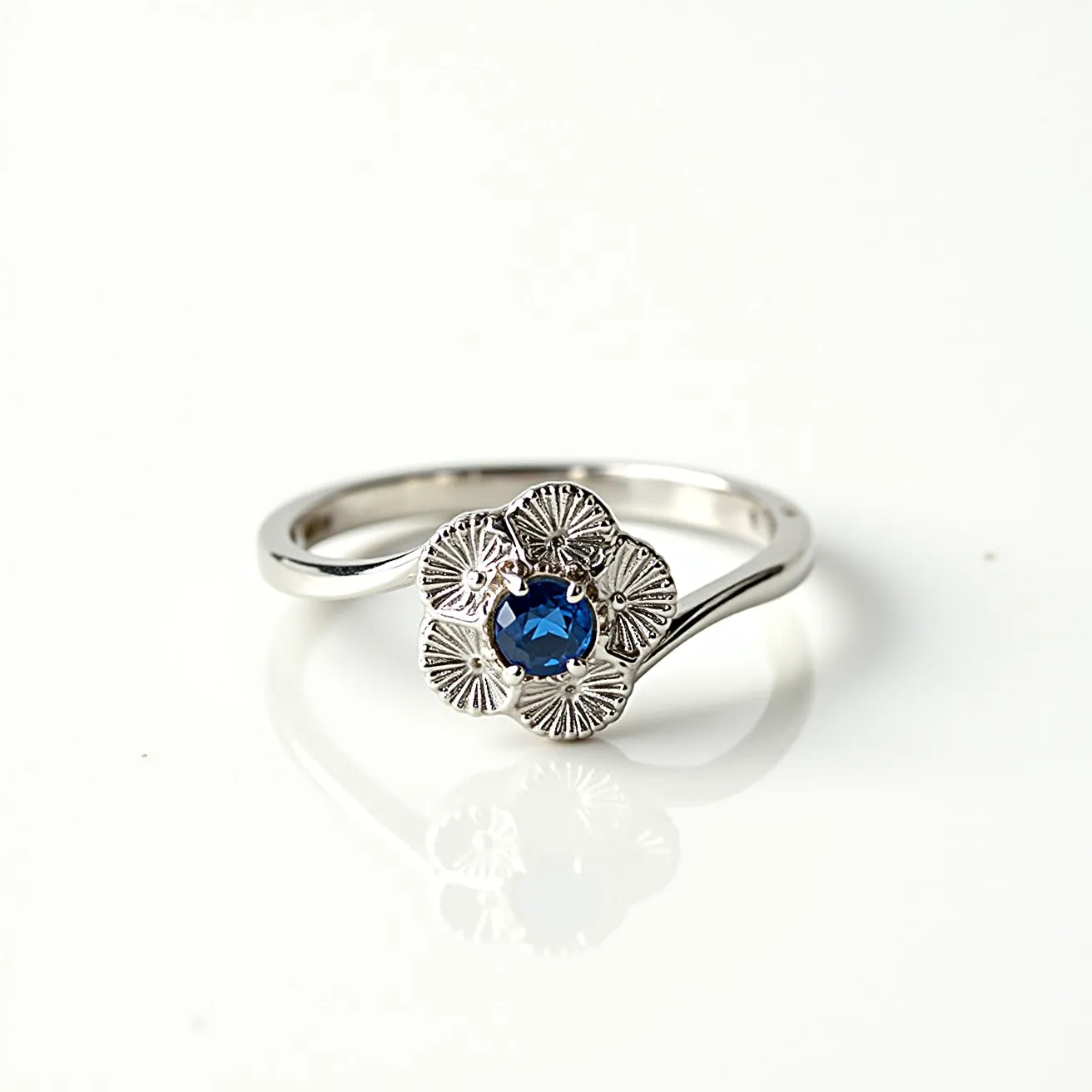 This rose ring features a delicate floral design with intricately detailed petals made of a silver-toned metal. At the center is a round, faceted blue gemstone, expertly set to enhance its brilliance. The band is smooth and slender, adding to the elegant simplicity of the piece. This combination of elements creates a harmonious balance between the metal and the gemstone, making the ring a refined and sophisticated accessory.