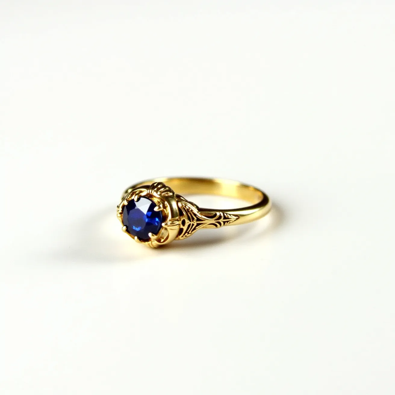 This rose ring features a stunning blue sapphire, cut in a round shape, set in an intricate gold band. The sapphire is securely held in place by a prong setting that enhances its brilliance and complements its deep hue. The design of the band includes delicate, floral-inspired detailing, adding to the elegance and sophistication of the piece. The choice of gold as the primary material gives the ring a warm and classic appearance, making it a timeless accessory.