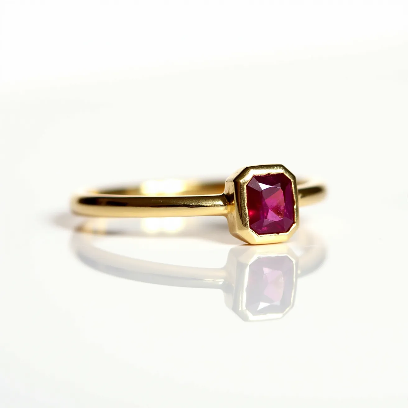 This ruby engagement ring features a striking emerald-cut ruby, showcasing its vibrant red hue. The gem is set in a bezel setting, which securely encases the ruby in gold, highlighting its geometric shape. The band is crafted from polished yellow gold, complementing the red of the ruby and providing a luxurious touch. The smooth finish of the band adds elegance and sophistication to the overall design.