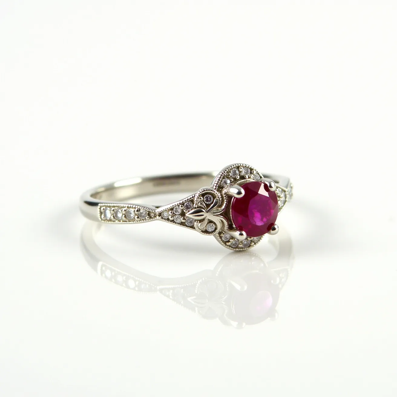 This ruby engagement ring features a striking round-cut ruby as the centerpiece, held securely in place by a delicate prong setting. The band is crafted from a reflective metal, likely white gold or platinum, and is adorned with small round diamonds that are intricately set along the shoulders. The detailed design includes milgrain embellishments that add a vintage touch, and floral motifs enhance the overall elegance of the ring. The combination of the vibrant ruby with the sparkling diamonds creates a timeless and sophisticated piece.