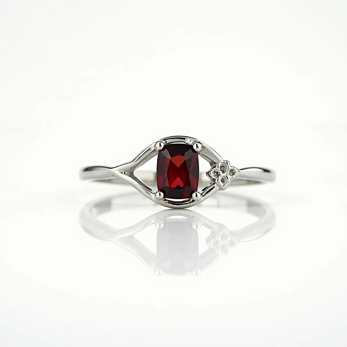 This ruby ring features a striking central gemstone, an oval-cut ruby, elegantly secured in a prong setting crafted from what appears to be a polished silver or white gold band. The vivid red of the ruby contrasts beautifully with the bright metallic hue of the band. Adding a touch of delicate charm, a small flower motif is gracefully incorporated next to the ruby, likely adorned with a tiny diamond or similar stone at its center, enhancing the ring's overall elegance. The band’s slender design emphasizes the ring's intricate details and the ruby’s rich, captivating color.