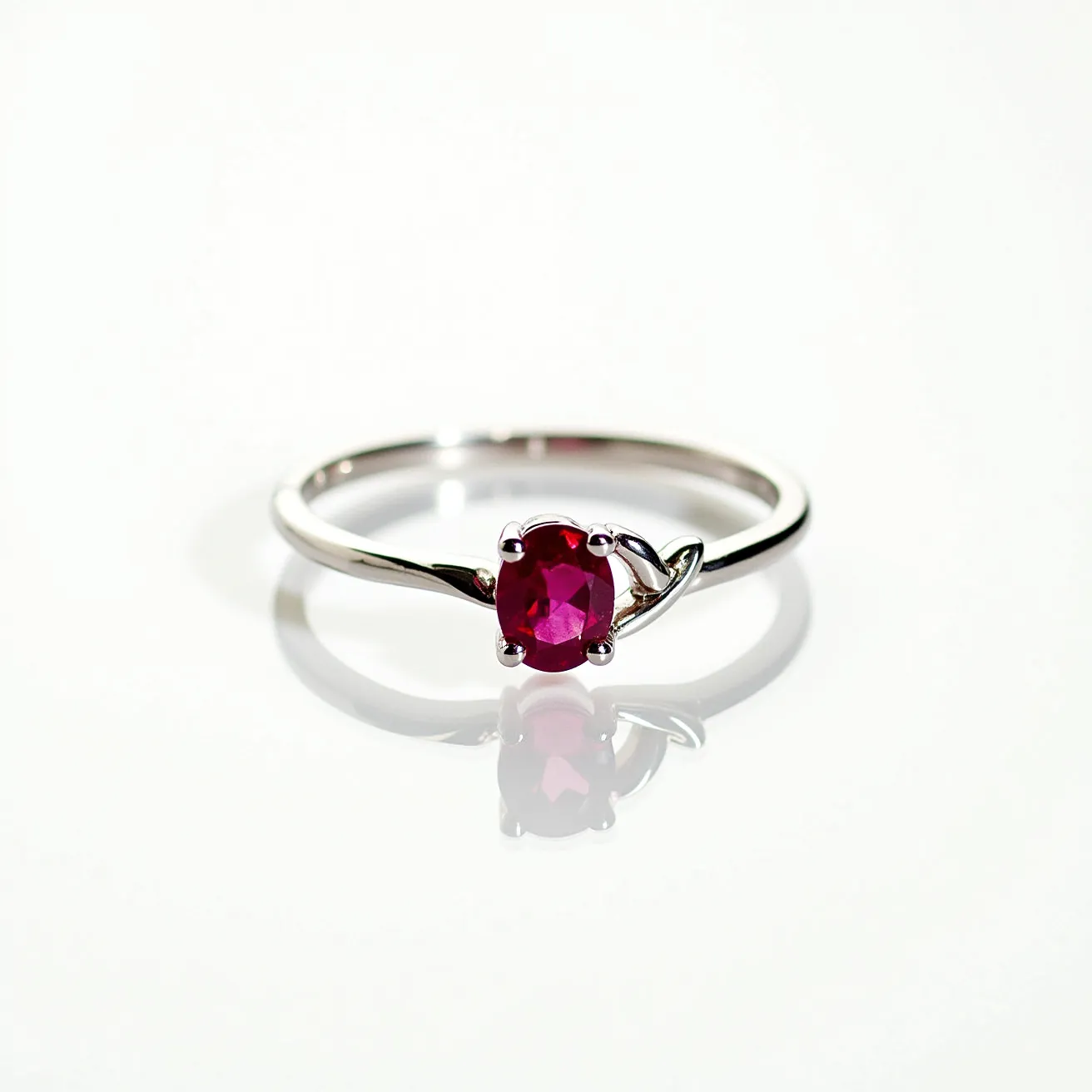 This ruby ring showcases an elegantly crafted design with a central oval-cut ruby set in a four-prong setting. The band is made from a polished metal, likely white gold or platinum, enhancing the ring's sophistication. A delicate twist in the band adds a subtle yet distinct design element that complements the vibrant red hue of the ruby. The setting securely holds the gemstone, ensuring it remains the focal point of the piece.