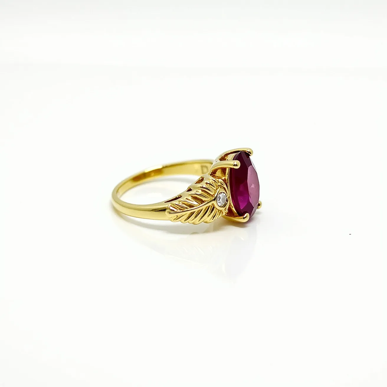 This ruby ring features a vibrant oval-cut ruby set in a prong setting that prominently displays the stone's brilliance. The band is crafted from gold, showcasing an elegant design with leaf motifs that extend from the central setting. Each side of the leaf design is accented with a small, round-cut diamond, adding a touch of sparkle and contrast to the piece. The overall craftsmanship highlights a harmonious blend of natural motifs with luxurious materials.