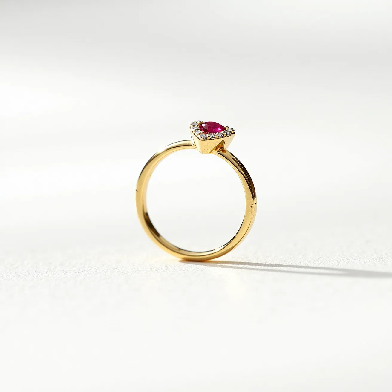 This ruby ring features a delicate gold band that supports a striking heart-shaped ruby as its centerpiece. The ruby is cut to enhance its vibrant red hue and is securely held in a prong setting. Surrounding the ruby are small, sparkling diamonds, adding a touch of brilliance and contrast to the central gemstone. The setting elevates the ruby slightly above the band, allowing light to pass through and accentuate its color and clarity. This exquisite combination of gold, ruby, and diamonds creates a timeless and elegant piece of jewelry.