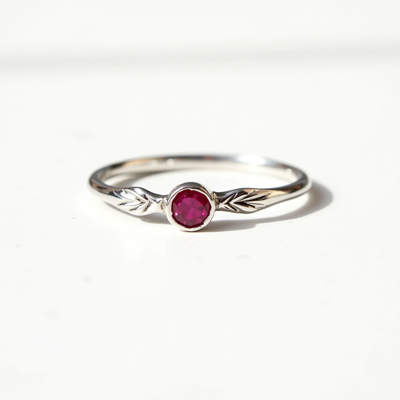 This ruby ring is crafted with a sleek silver band, elegantly adorned with intricate leaf details on either side of the central gemstone. The centerpiece is a vibrant, round-cut ruby, securely set in a bezel setting that highlights its deep red hue. The minimalist design of the band complements the ruby's rich color, creating a harmonious balance of simplicity and sophistication. The silver material enhances the overall elegance of the ring while providing a durable setting for the gemstone.