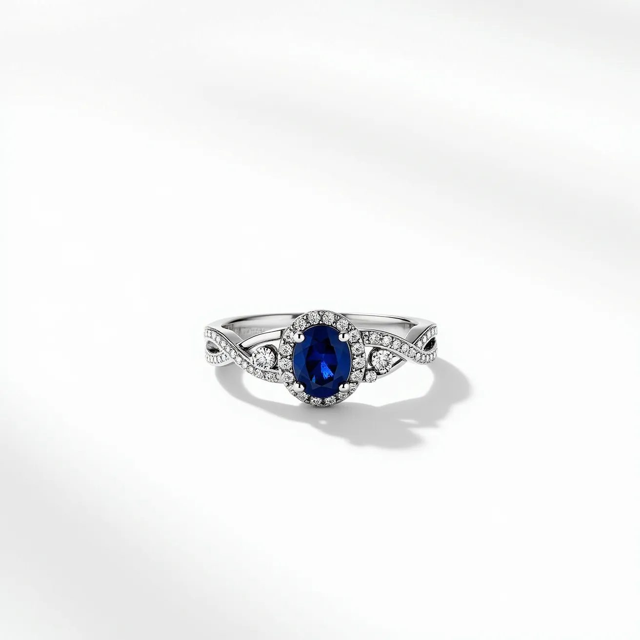 This sapphire ring features a stunning deep blue oval-cut sapphire as the centerpiece, encircled by a halo of small, round brilliant-cut diamonds that enhance its brilliance. The band, crafted from a lustrous white metal, possibly white gold or platinum, incorporates an elegant design with interwoven diamond accents, providing a sophisticated twist to the classic style. The sapphire is securely held in place by prongs, ensuring both visibility and safety. The elegant combination of the vivid sapphire and the sparkling diamonds creates a harmonious blend of color and light, making this ring a captivating piece of jewelry.