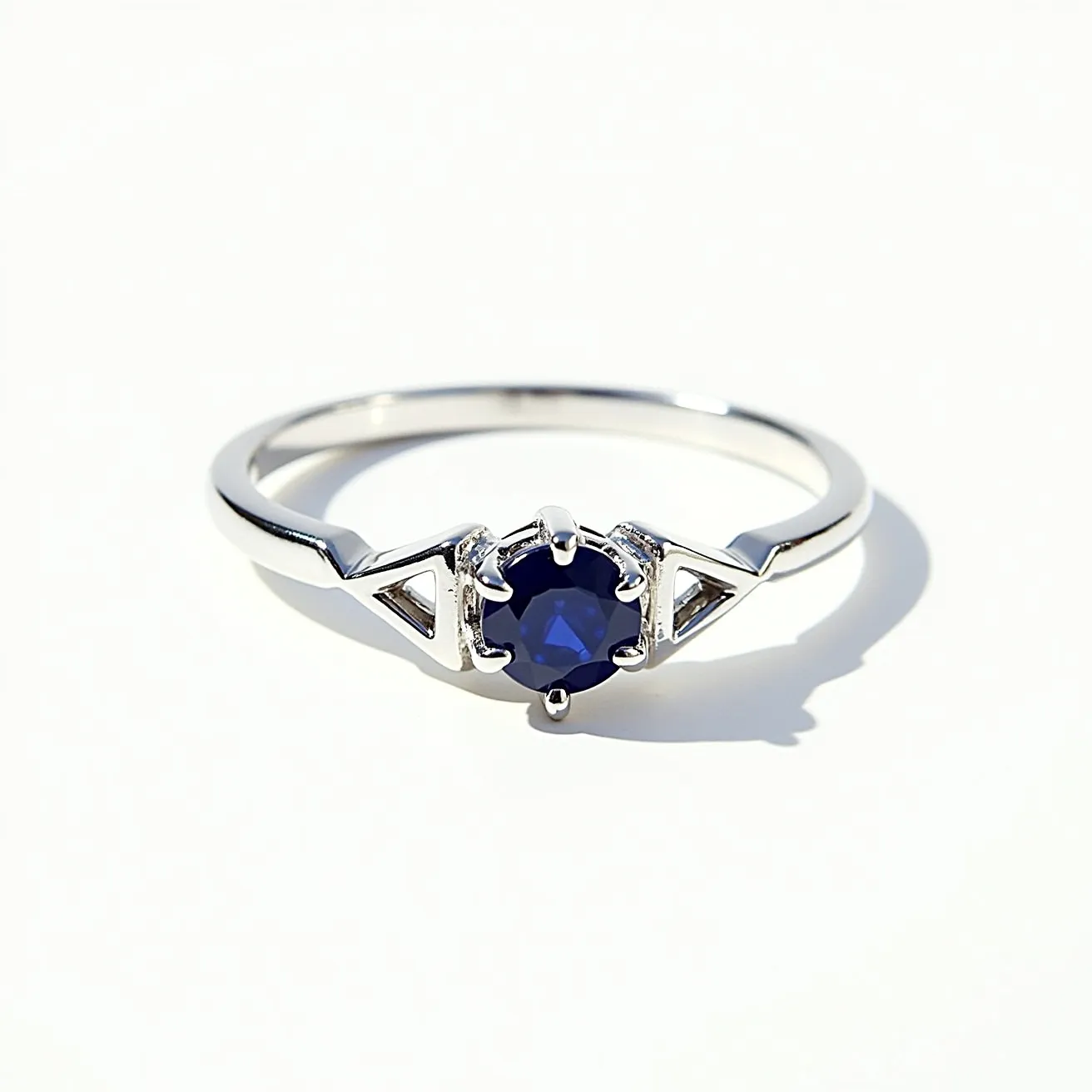 This sapphire ring features a striking deep blue round-cut sapphire set at its center in a six-prong setting, which not only secures the gemstone but also allows it to catch light beautifully from various angles. The band appears to be made of a polished white metal, likely platinum or white gold, enhancing the elegance and modern aesthetic of the piece. The design on either side of the central stone incorporates geometric shapes, adding an element of sophistication to the overall design. The simplicity and refinement of the clasp-free design emphasize the natural beauty and allure of the sapphire itself.