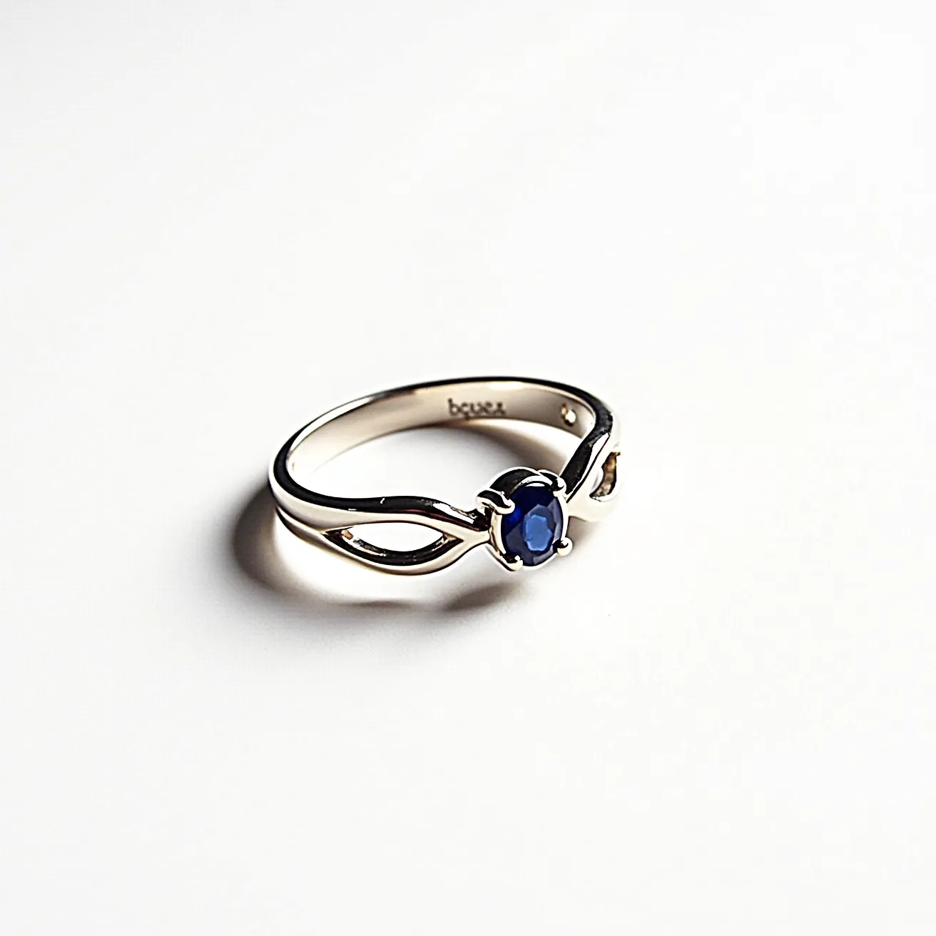 This sapphire ring features a polished band crafted from what appears to be a high-quality metal, potentially white gold or platinum, giving it a sleek and elegant appearance. At its center, an oval-shaped sapphire, rich in color, is securely set within a four-prong setting that showcases the gem beautifully. The design includes a delicate twist in the band on either side of the gemstone, adding a modern and stylish flair to the ring's overall aesthetic.