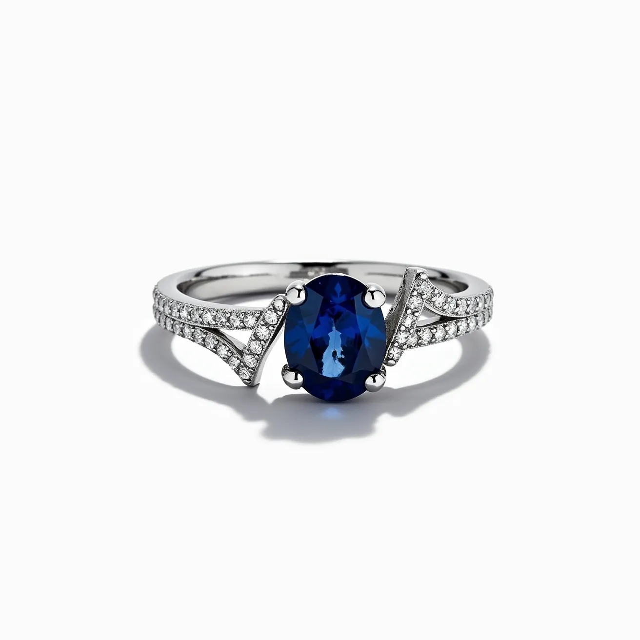 This sapphire ring features an exquisite oval-cut blue sapphire as its centerpiece, set elegantly with four prongs. It is flanked by a series of smaller round-cut diamonds arranged in a split shank style, adding a brilliant shimmer to the overall design. The band is crafted from a lustrous metal, likely white gold or platinum, providing a sleek and sophisticated backdrop that highlights the vivid blue hue of the sapphire. The intricate setting and meticulous arrangement of diamonds enhance the ring's elegance, making it a striking piece of jewelry.