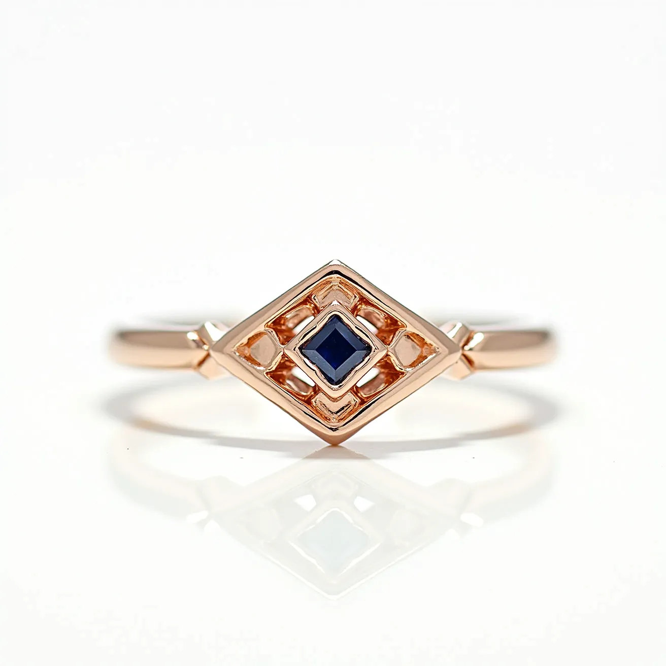 This sapphire ring features a central blue sapphire gem that is cut into a square shape and securely set in a geometric, openwork design. The band and setting are crafted from a warm-toned metal, likely rose gold, which complements the deep blue of the sapphire. The ring's unique design emphasizes a symmetrical, diamond-shaped framework, enhancing the modern elegance of the piece. The sapphire is held in place by a bezel setting, providing both security and a sleek appearance. The simplicity of the band accentuates the intricate design and vibrancy of the gemstones.