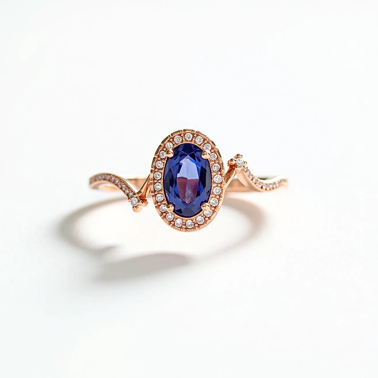 This sapphire ring features an oval-cut blue sapphire as its centerpiece, surrounded by a delicate halo of small, round-cut diamonds. The band is made of rose gold, adding a warm and elegant tone to the overall design. The diamonds are set in a pave style along the twining band, enhancing the ring's sophistication and sparkle. The setting securely holds the sapphire with prongs, ensuring its stability and prominence. The blend of the blue sapphire, rose gold, and sparkling diamonds creates a harmonious and refined aesthetic.