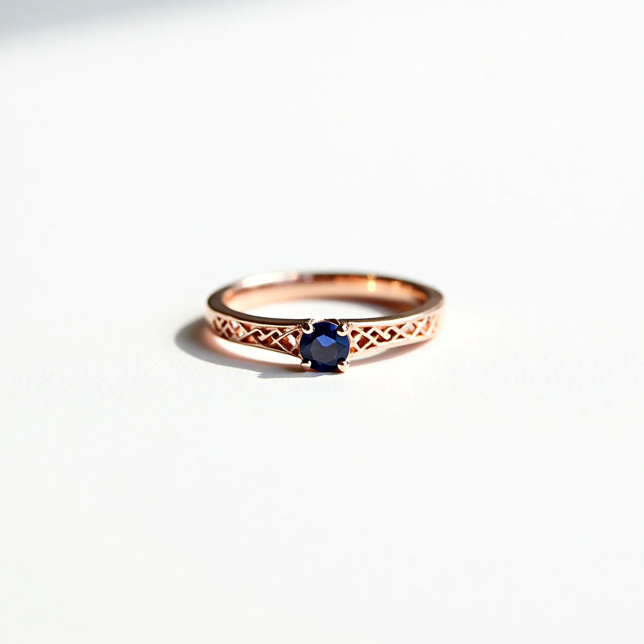 This sapphire ring features a vibrant, round-cut blue sapphire set in a delicate rose gold band. The band showcases an intricate lattice design, adding an element of elegance and sophistication to the piece. Secured by a prong setting, the sapphire is prominently displayed, highlighting its deep color and brilliance. The craftsmanship of the band’s design complements the gemstone perfectly, making it a striking and luxurious accessory.