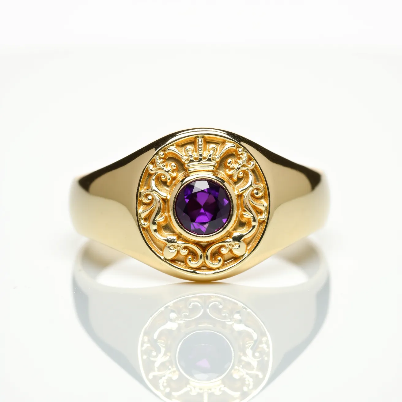 This signet ring features a gold band with a detailed crest design on its face, intricately carved with ornate scrollwork and a prominent crown motif. At the center of the crest lies a round-cut purple gemstone, likely an amethyst, securely set within a bezel setting. The ring displays a sleek, polished finish that enhances the elegance of the materials and craftsmanship.