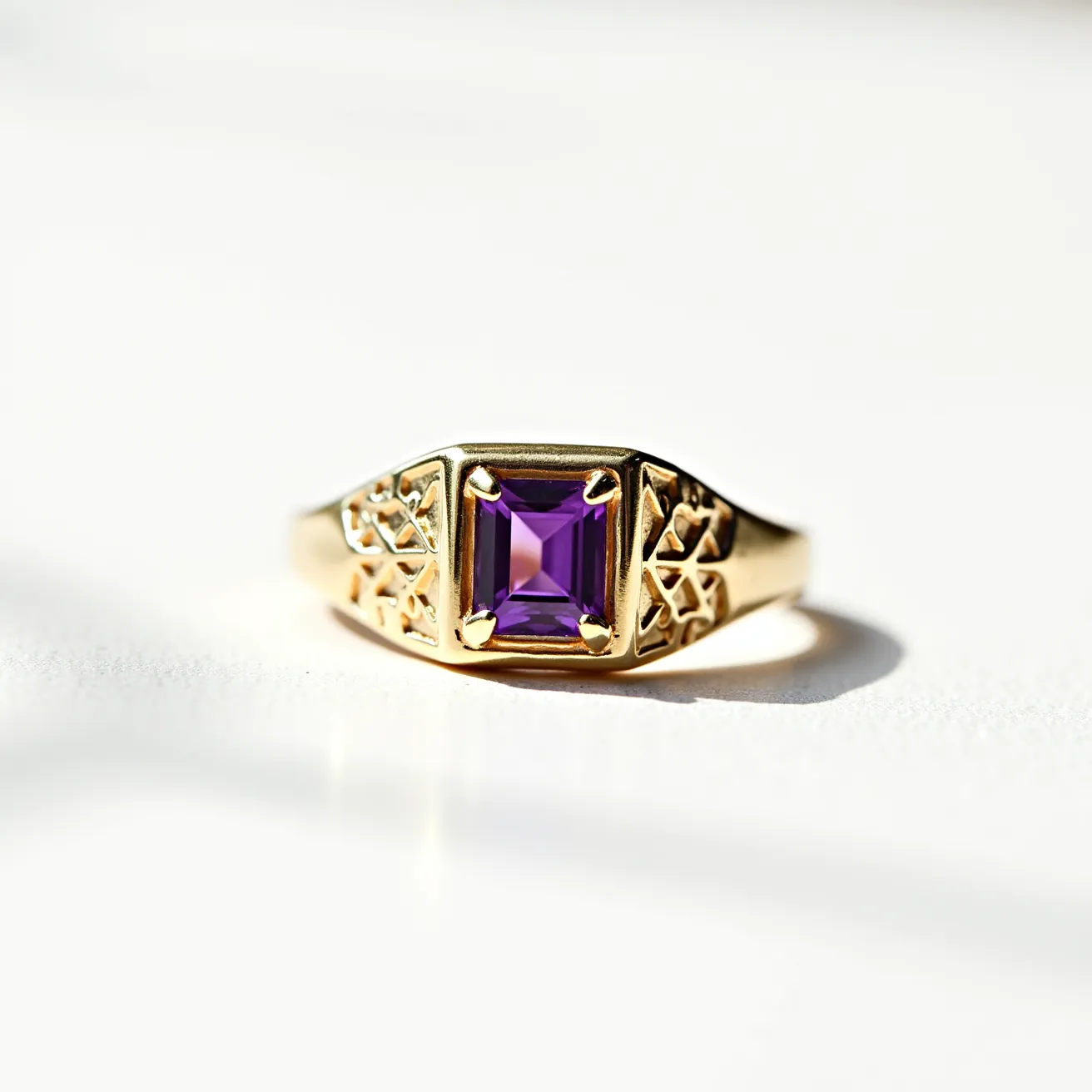 This signet ring features a square-cut purple gemstone prominently set within a bezel setting, providing a secure and stylish centerpiece. The ring is crafted from gold, with a polished finish that enhances its luxurious appearance. The shoulders of the ring have intricate, decorative patterns that add complexity and elegance to the overall design. The ring's design is seamless, with no visible clasps or attachments, ensuring a smooth and continuous aesthetic.