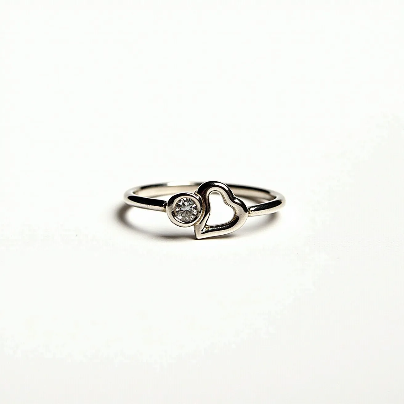 This silver heart ring is crafted from polished silver, featuring a delicate band that holds a charming open heart design. Adjacent to the heart is a round-cut gem, securely set in a bezel setting, which adds a touch of sparkle and elegance. The simplicity and elegance of the design make it a versatile piece suitable for various occasions.