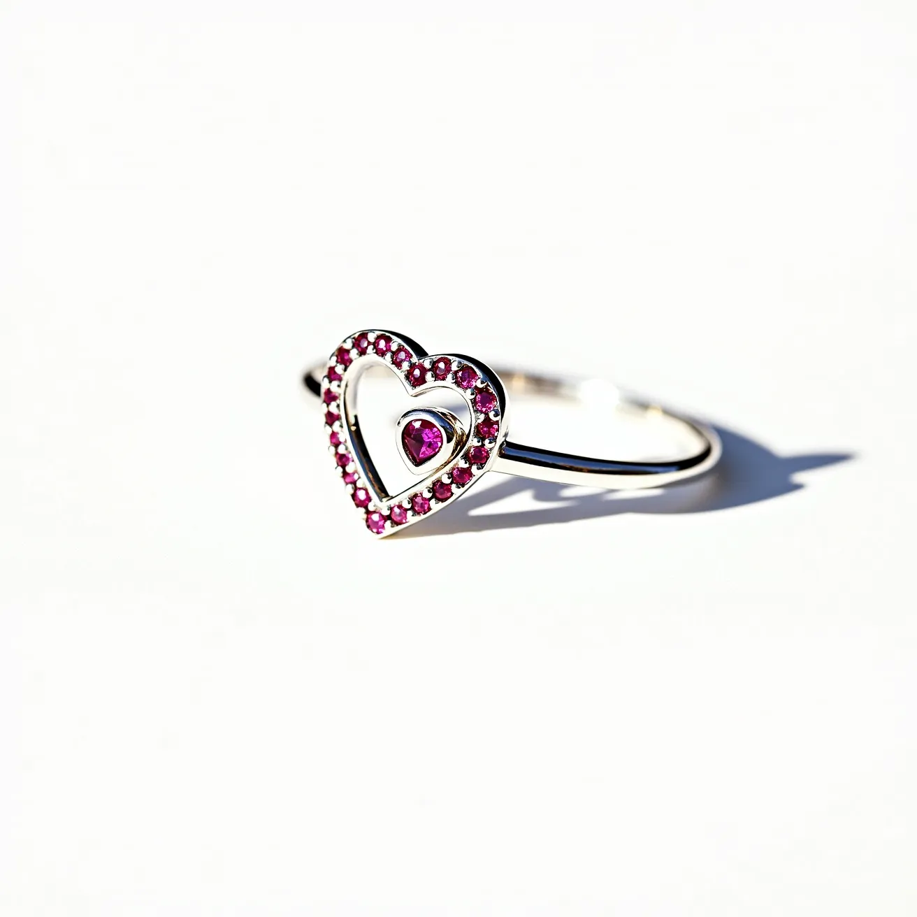 This silver heart ring features a delicate band crafted from what appears to be silver. The centerpiece of the ring is a charming heart-shaped design, adorned with small, round, pink gemstones that encircle the outer edge, casting a vivid hue that complements the metal's shine. At the center of the heart motif, there is a single, larger round pink gemstone, elegantly set in a simple bezel setting that secures it in place while allowing maximum sparkle. The intricate detailing of the stones and the precise setting contribute to the ring's graceful design, creating a visually appealing piece of jewelry.