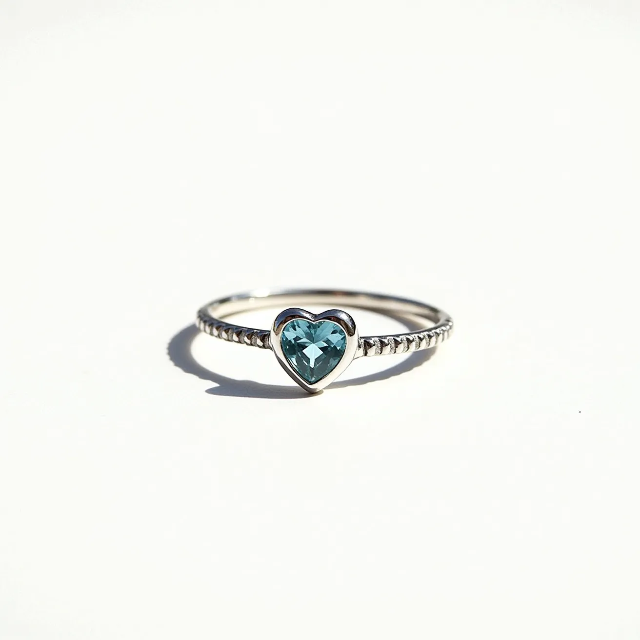 This silver heart ring features a delicate band crafted from polished silver, showcasing a simplistic yet elegant design. At its center, the ring holds a heart-shaped gemstone, possibly a blue topaz or aquamarine, that is intricately faceted to catch the light and enhance its brilliance. The stone is securely set in a bezel setting, which provides a smooth, protective edge around the gem, allowing for everyday wear without compromising on style. The band itself is adorned with a subtle braided pattern, adding an extra touch of texture and intrigue to the overall aesthetic of the piece.