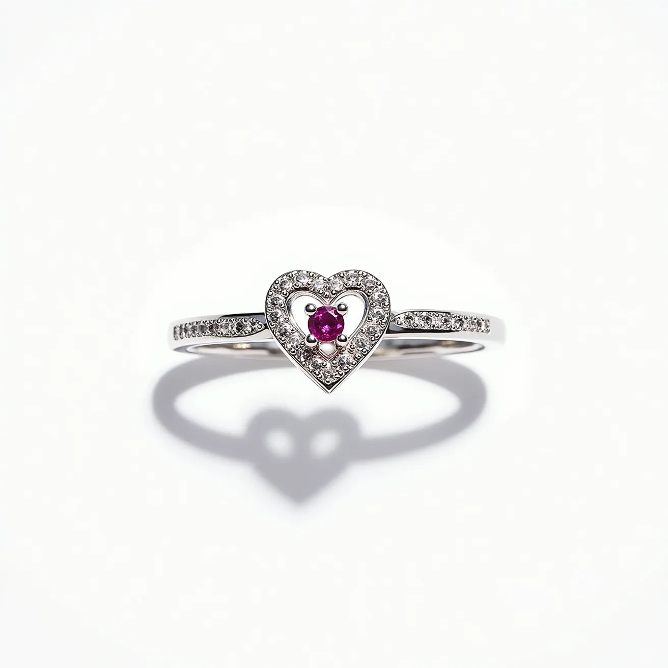 This silver heart ring features a delicate heart design as its focal point. The ring is crafted from polished silver, providing a sleek and reflective finish. Embedded within the heart is a central pink gemstone, likely a round-cut ruby, held securely in a prong setting. Surrounding the heart and lining the band are small, clear gemstones, presumably diamonds or cubic zirconias, set in a pave setting that adds an additional layer of sparkle. The band is slender and enhances the elegant and refined appearance of the ring.