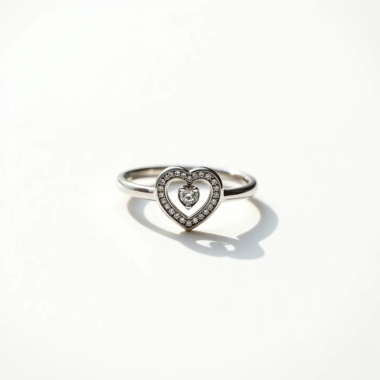 This silver heart ring features a polished silver band and a heart-shaped design at its center, adorned with small, sparkling gems. The heart outlines a larger open heart shape, with the inner heart encircling a round-cut central stone. The stones are prong-set, highlighting their brilliance and providing an elegant contrast against the silver. The overall setting gives the ring a balanced appearance, and it seamlessly integrates the stones without any visible clasps or attachments, emphasizing simplicity and elegance in its design.