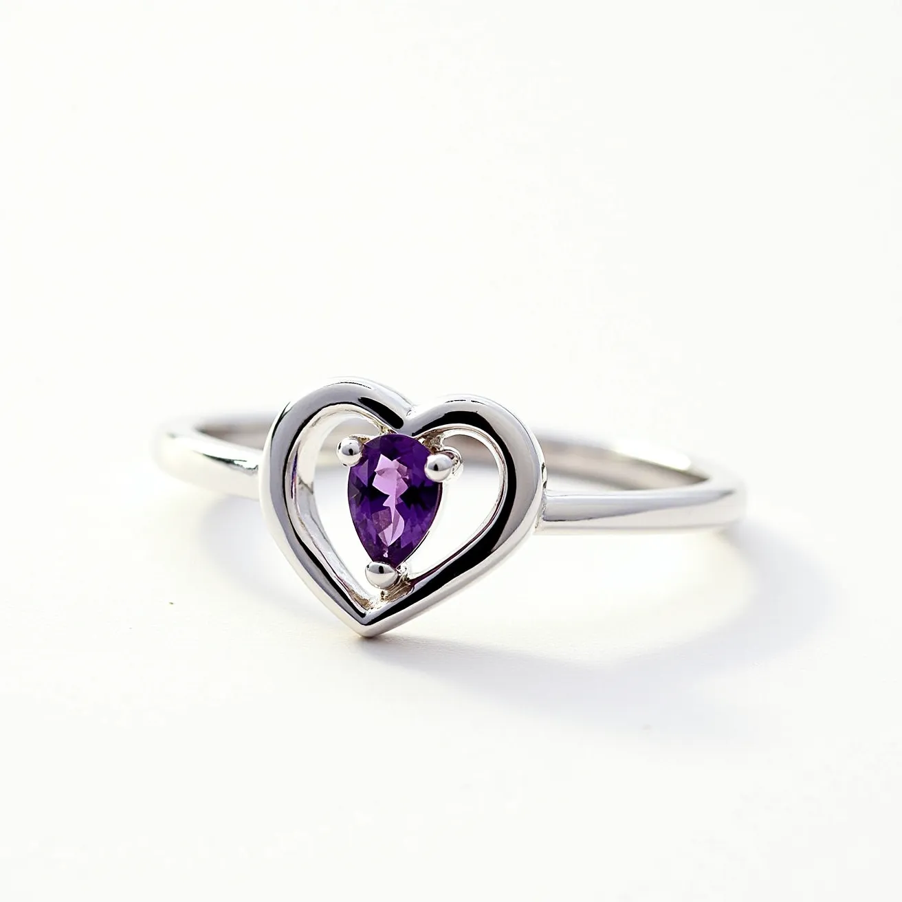 This silver heart ring features a delicate heart-shaped design crafted from polished silver. At the center of the heart is a pear-cut purple gemstone, likely an amethyst, held securely in place by a four-prong setting. The band is sleek and smooth, complementing the elegance of the heart and stone centerpiece. The simplicity of the design emphasizes the sparkle of the gemstone, creating a harmonious balance between the metal and the gem.