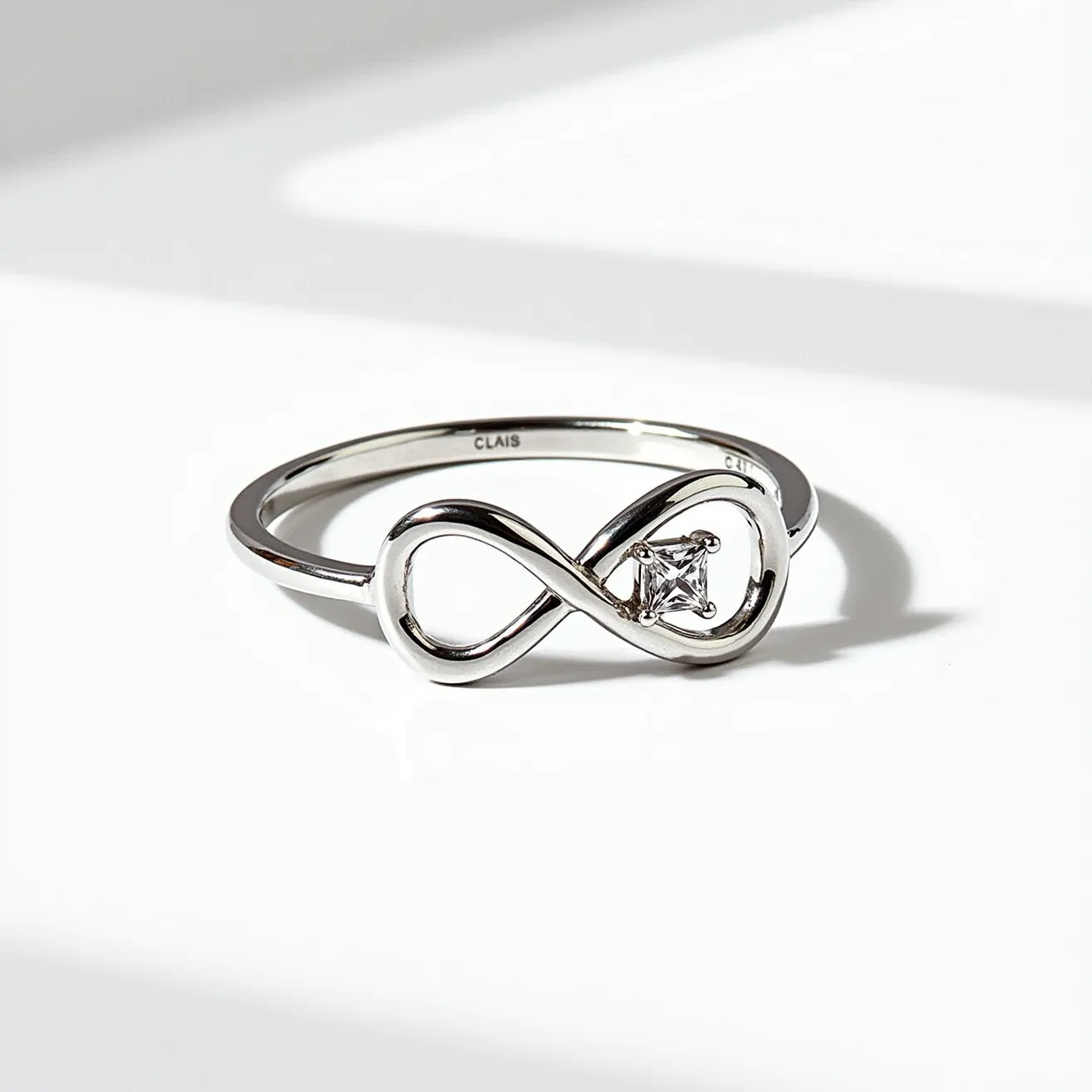 This silver promise ring features an elegant infinity symbol as its central design, crafted from polished silver. Nestled within the flowing curves of the infinity loop is a square-cut gemstone, securely set in a four-prong setting. The simple band complements the overall sleek and modern aesthetic, making the ring both symbolic and stylish.