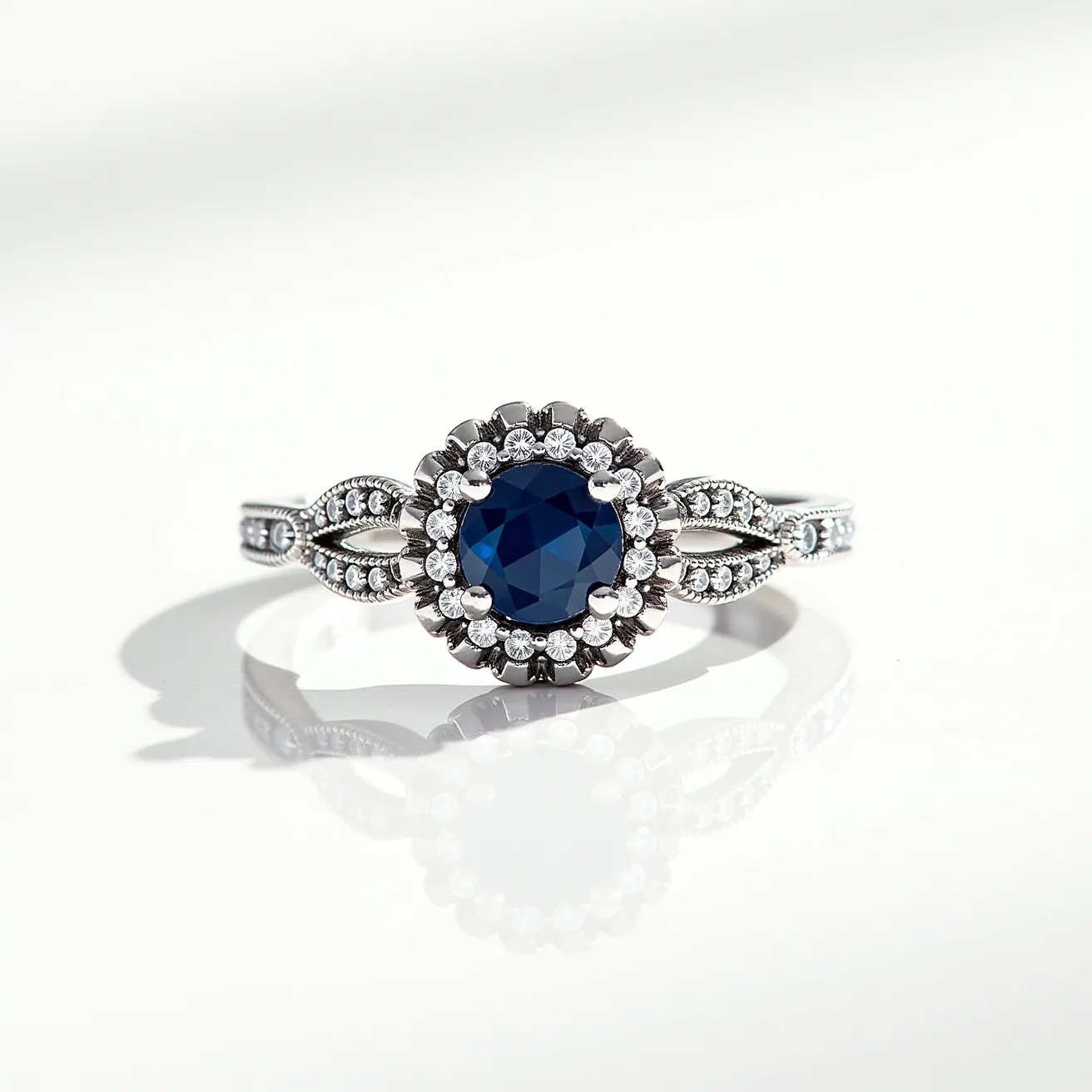 This silver promise ring features a prominent round blue gemstone at its center, elegantly set with a halo of small round clear stones that enhance its brilliance. The band of the ring is crafted from silver and exhibits intricate detailing along the sides, which beautifully complements the central setting. Each side of the band displays a delicate pattern adorned with additional small clear stones, adding to its refined appearance. The ring's overall design is both ornate and graceful, with the blue stone providing a striking contrast to the bright silver and clear stones.