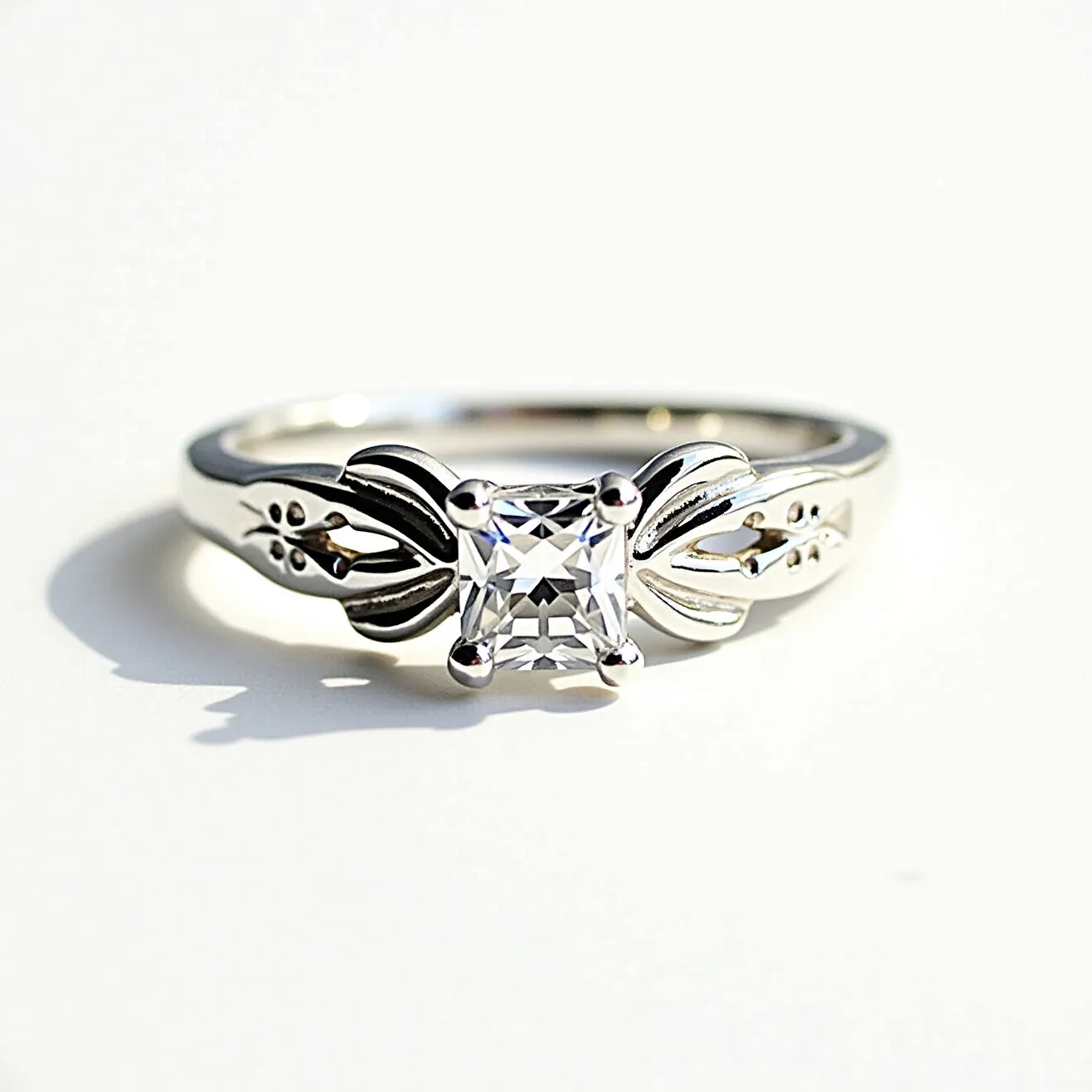 This silver ring features a striking square-cut gemstone set in a classic four-prong setting, which securely holds the stone while allowing maximum light to enter and reflect. The band is crafted from silver and is adorned with intricate floral motifs on either side of the gemstone, adding a touch of elegance and sophistication to the overall design. The smooth finish and polished appearance of the silver enhance the ring's lustrous appeal, making it a captivating piece of jewelry.