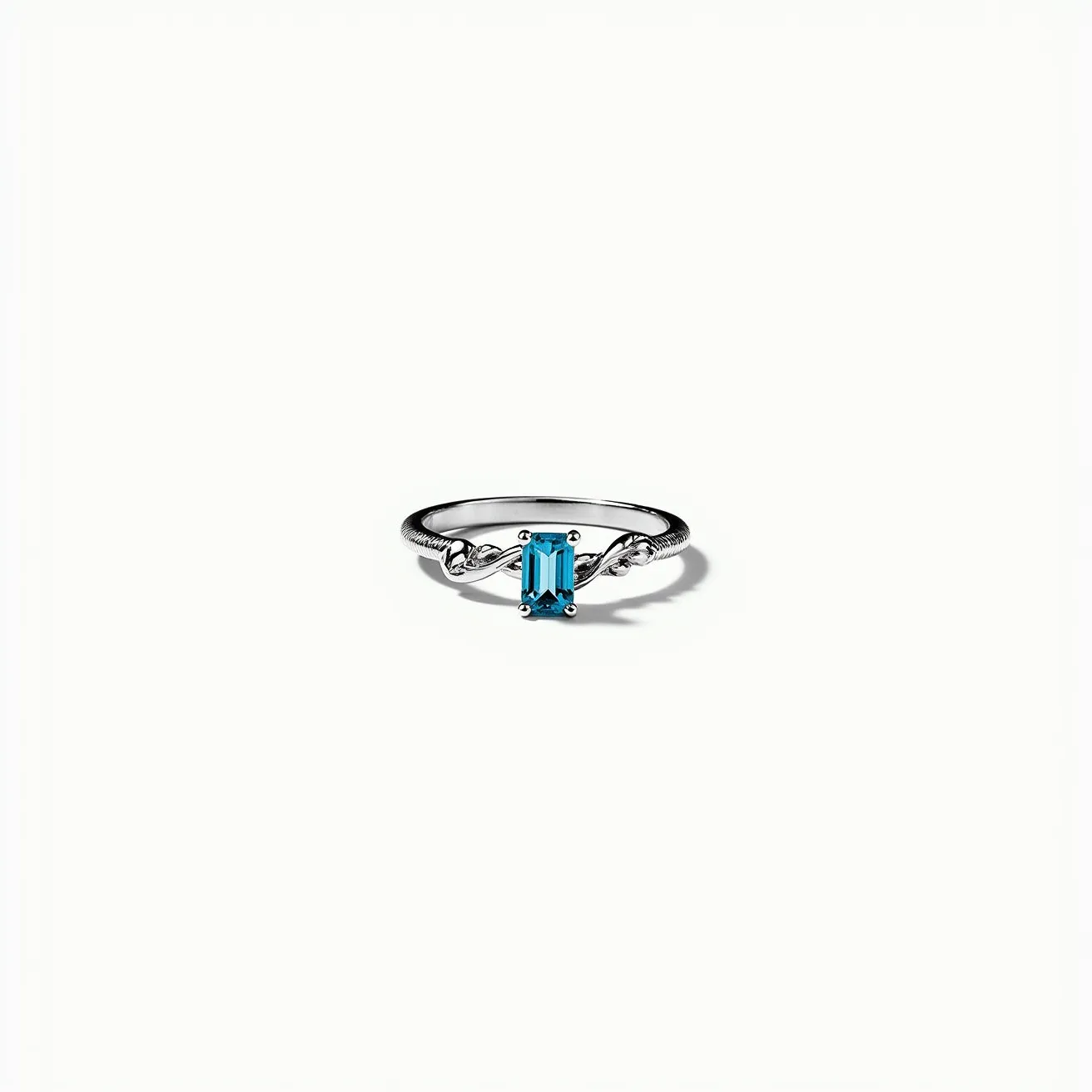 This silver ring features an elegant design with an emerald-cut blue gemstone as its centerpiece. The gem is held securely by a four-prong setting that accentuates its clarity and vibrant color. The band showcases a delicate twist pattern, adding a touch of sophistication and visual interest to the piece. The simplicity of the setting highlights the gemstone, making it the focal point of the ring, while the polished silver band provides a classic and timeless appeal. This combination of materials and design elements results in a refined piece of jewelry suitable for various occasions.