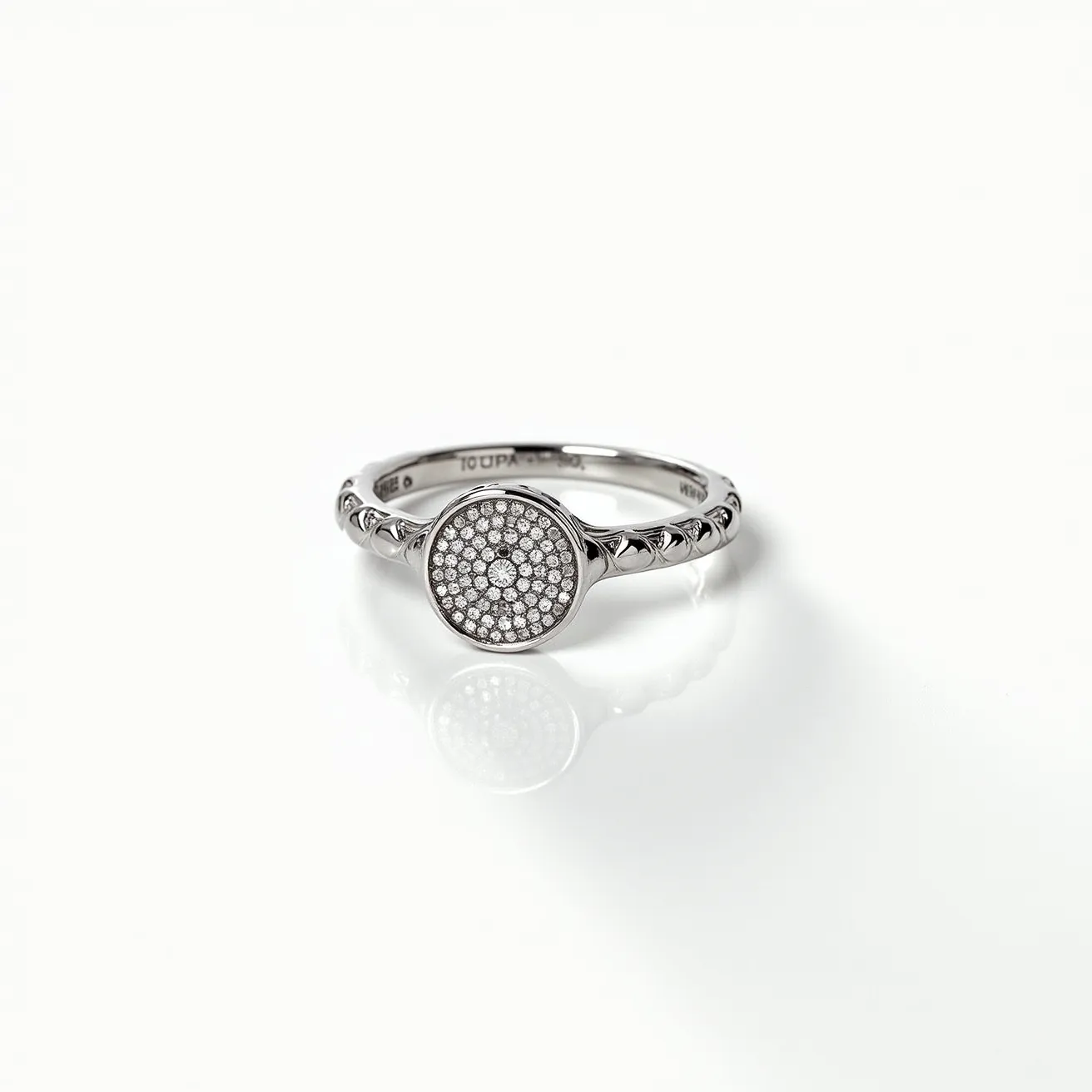 This silver ring features a round centerpiece encrusted with numerous small, round-cut gems, likely diamonds, set in a pavé setting which adds a sparkling, textured surface to the design. The band is adorned with a series of engraved patterns that provide an elegant embellishment and enhance the overall aesthetic of the ring. The materials appear to be high-quality silver, and there is no visible clasp, suggesting a traditional circular band design for ease and style in wearing.