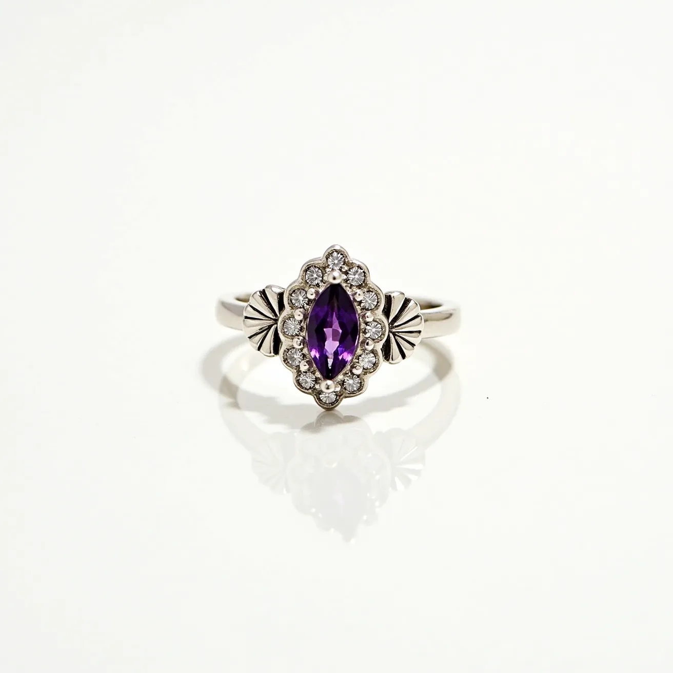 This silver ring features a marquise-cut purple gemstone set at its center, surrounded by a halo of small, round clear stones. The central gem is securely held in place with a prong setting that enhances its brilliance. The band of the ring is adorned with decorative silver details flanking the central setting, adding a touch of elegance. The ring's design integrates both the gemstone and metalwork harmoniously, offering a classic yet distinctive look.