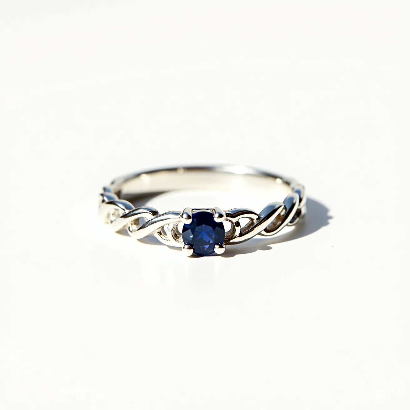 This silver wedding ring features an elegant band crafted from lustrous silver material, intertwined in a graceful twisted design. At its center, the ring showcases a stunning deep blue sapphire, cut in a brilliant round shape, enhancing its captivating sparkle. The sapphire is securely held in place by a classic prong setting, which not only secures the gem but also allows light to pass through, maximizing its brilliance. The ring combines simplicity with sophistication, making it a timeless piece for a wedding collection.