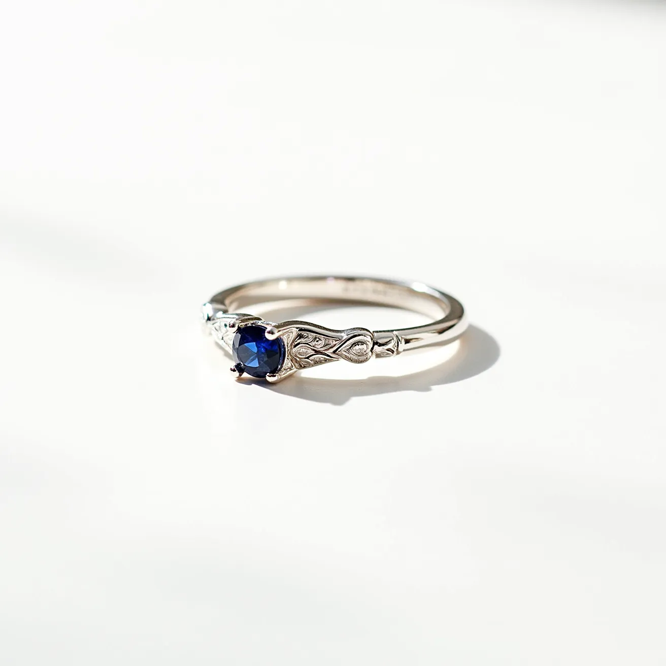 This silver wedding ring features a striking blue gemstone, likely a sapphire, which is round-cut and set in a secure prong setting. The silver band is elegantly designed with intricate detailing that enhances the overall aesthetic. The ring does not have any additional clasps or attachments, maintaining a streamlined and sophisticated look.