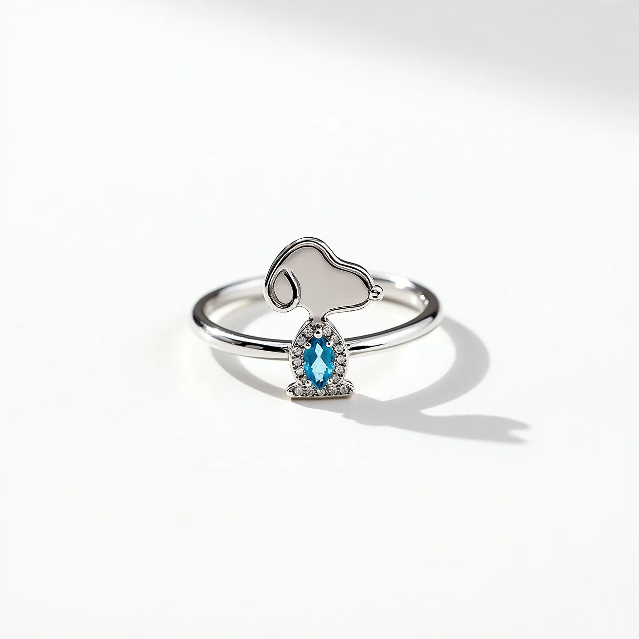 This Snoopy ring features a sleek design crafted from polished silver metal, forming the iconic outline of Snoopy's head. The central focal point is a marquise-cut blue gemstone, securely set in a halo of small, shimmering clear stones, adding sparkle and a touch of elegance to the piece. The band is smooth and minimalist, ensuring comfort and understated style. There is no visible clasp or additional attachments, emphasizing the simplicity and charm of the design.