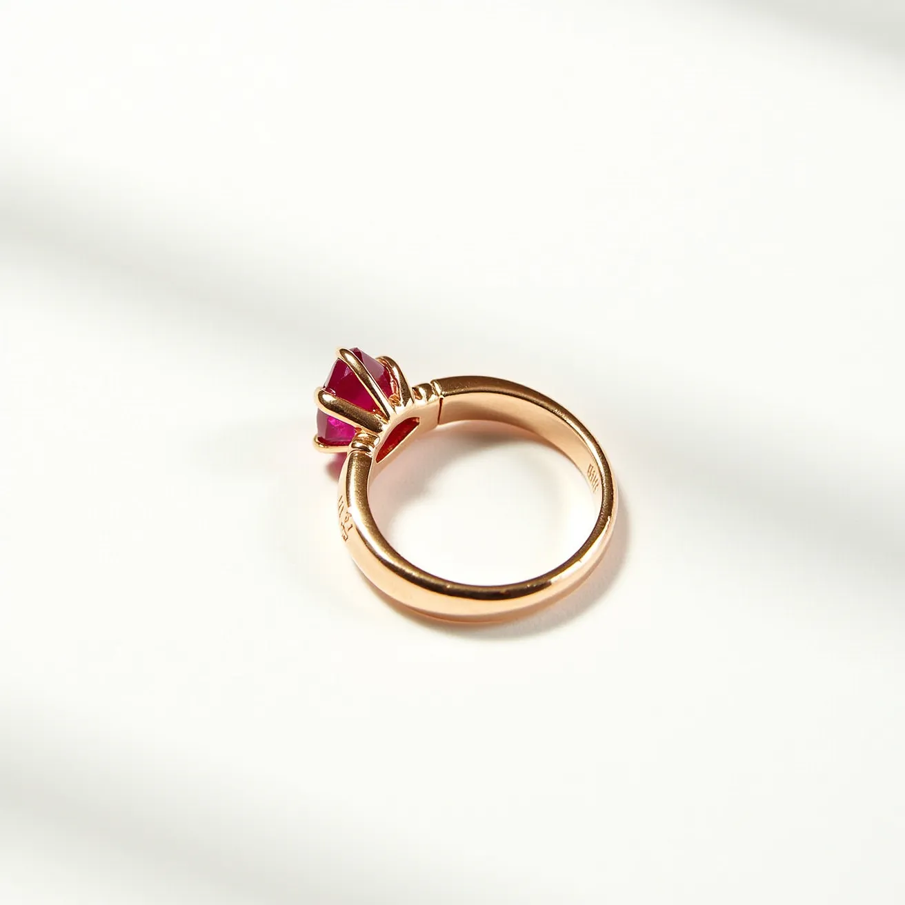 This solitaire ring features a vibrant red gemstone, expertly cut in a pyramid shape and securely set in an elegant gold band. The setting is a prong design, which elegantly holds the gemstone in place while allowing maximum light exposure for enhanced brilliance. The gold band has a polished finish, complementing the warm hue of the gemstone. The ring's overall design is both timeless and sophisticated, showcasing a classic solitaire style with a touch of modern flair.