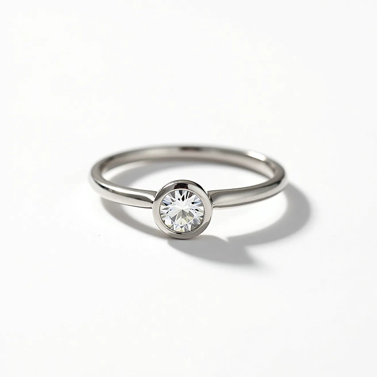 This solitaire ring features a sleek and polished band, likely made of a high-quality metal such as white gold or platinum, showcasing its elegant simplicity. The centerpiece is a round brilliant-cut diamond, securely set in a bezel setting that encircles the stone entirely, ensuring both protection and a modern aesthetic. The setting highlights the diamond's brilliance while maintaining a seamless appearance without any additional embellishments or attachments.