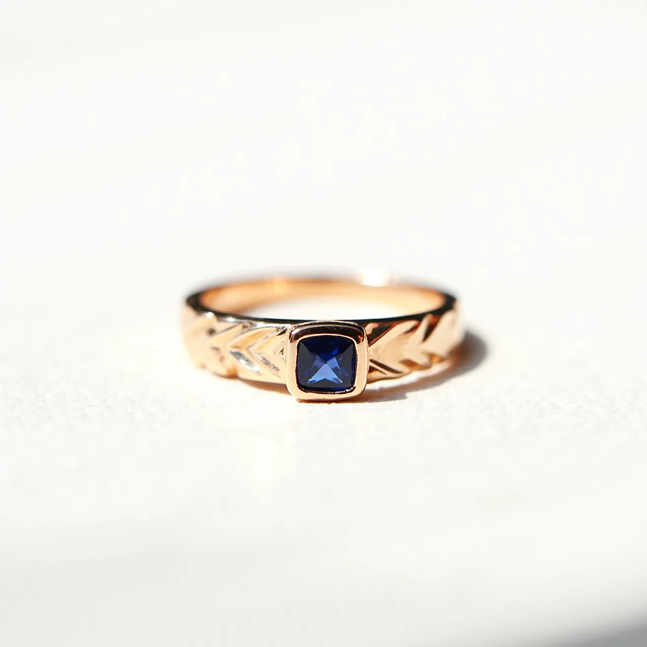 This Solomon's ring features a gold band with intricate leaf-like engravings along its surface, adding a touch of elegance to the piece. Set in the center is a square-cut blue sapphire, securely held in a bezel setting that complements the ring's overall design. The combination of gold with the deep blue gem creates a striking and timeless aesthetic, making it a distinguished accessory.