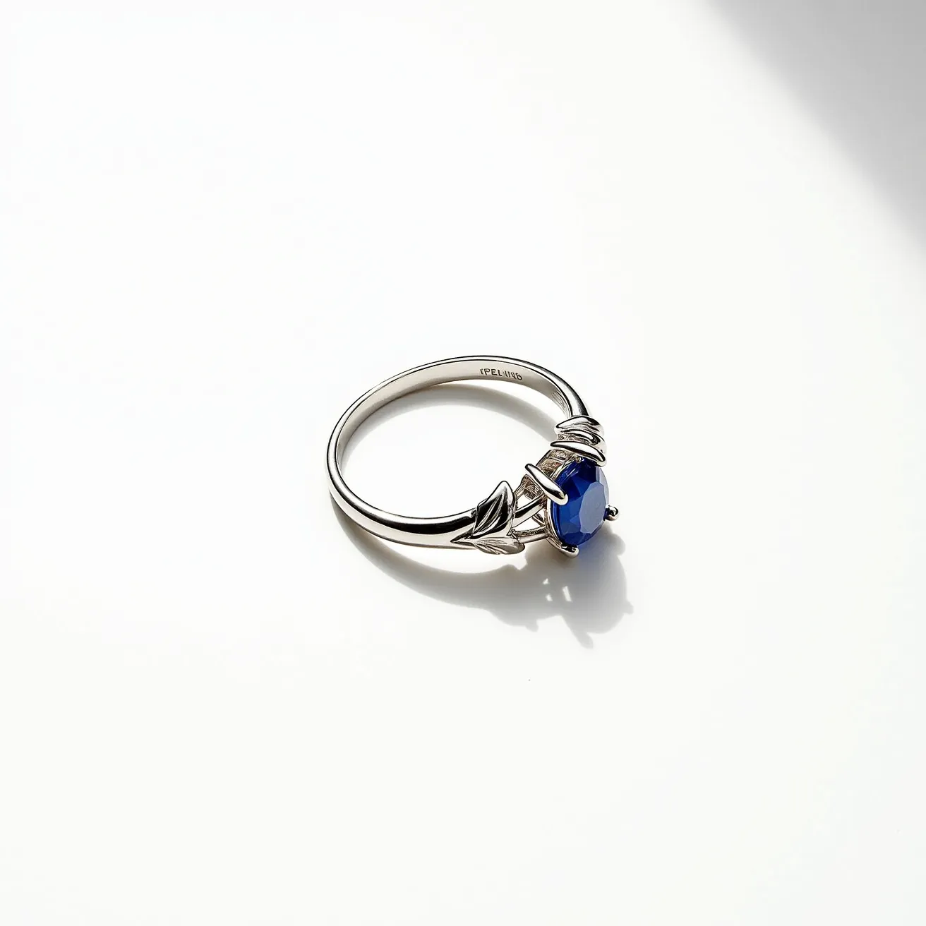 This Solomon's ring features a central, oval-cut blue gem, likely a sapphire, set prominently in the band. The gem is held in place by delicate prongs in a classic setting, enhancing its visibility and brilliance. The band is made of a reflective, silver-toned metal, possibly sterling silver. Ornate leaf-like designs flank the gem, adding elegance to the piece without interrupting its symmetry. The inner band is engraved with the word "IRELAND," indicating possible origin or inspiration.